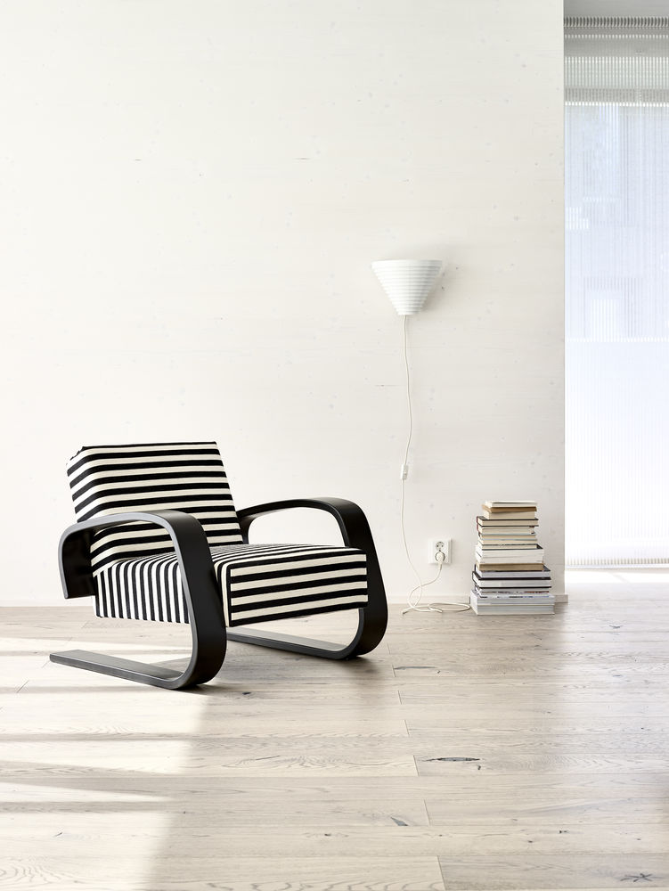 Helle minimalistische Szene mit Artek A910 Wandleuchte, Sessel mit Streifenmuster und Bücherstapel.