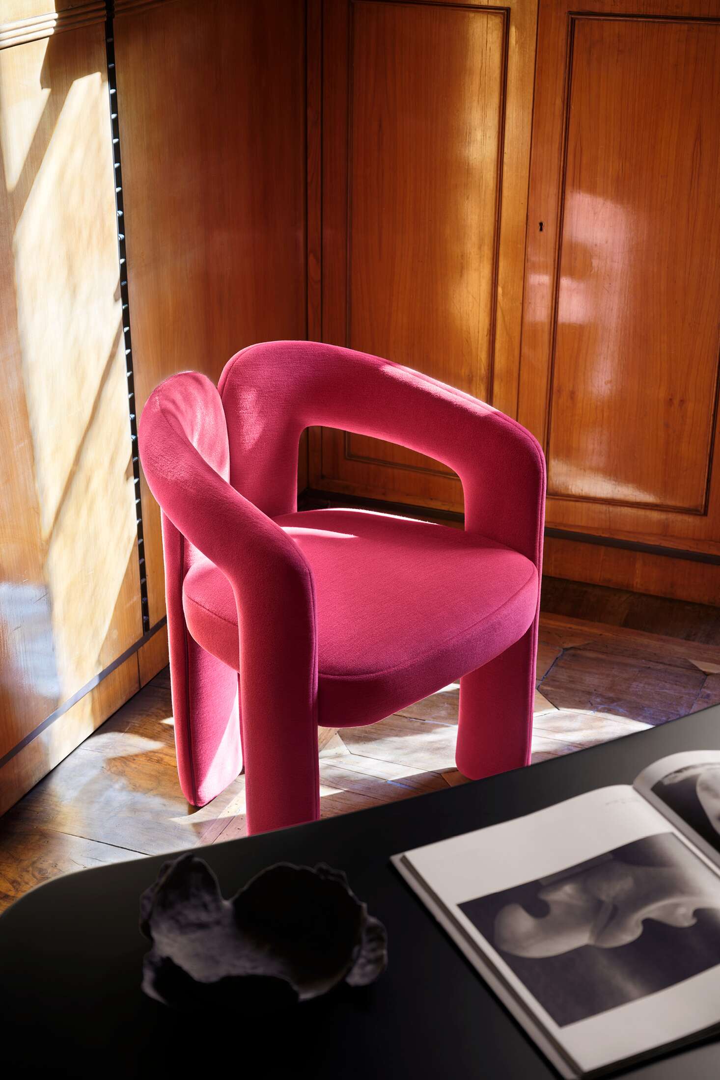 Nahaufnahme des Cassina 562 Dudet Sessels in Pink vor einer Holzwand, modernes Möbeldesign.