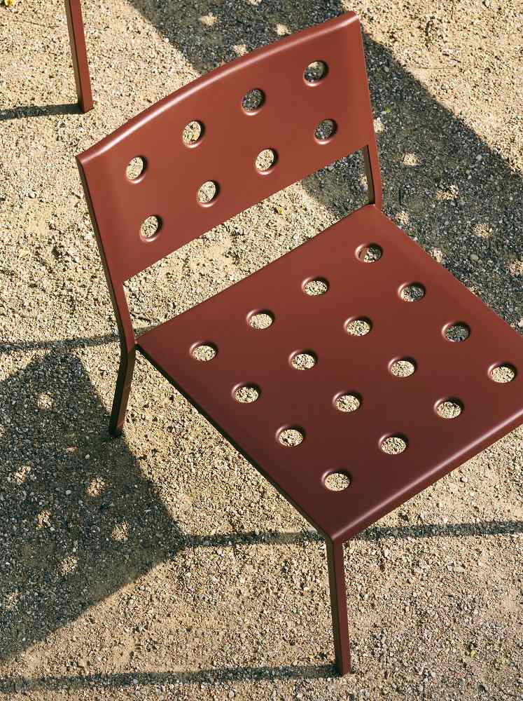 Nahaufnahme des braunen Hay Balcony Outdoor Lounge Chair Stuhls mit runden Löchern auf Kiesboden.