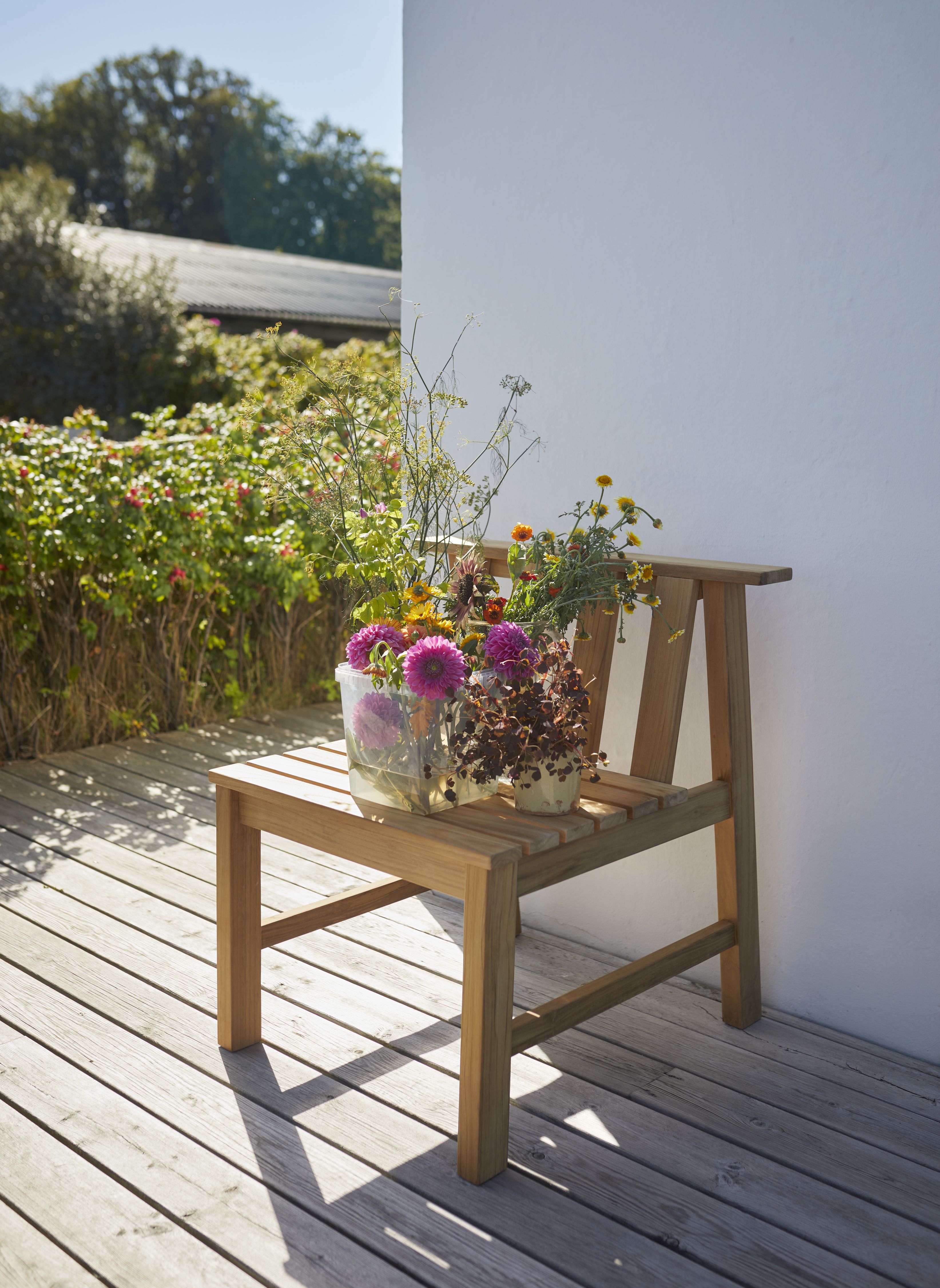 Cadence Stuhl Teak Outdoor von Skagerak by Fritz Hansen mit Blumen auf einer Holzterrasse.