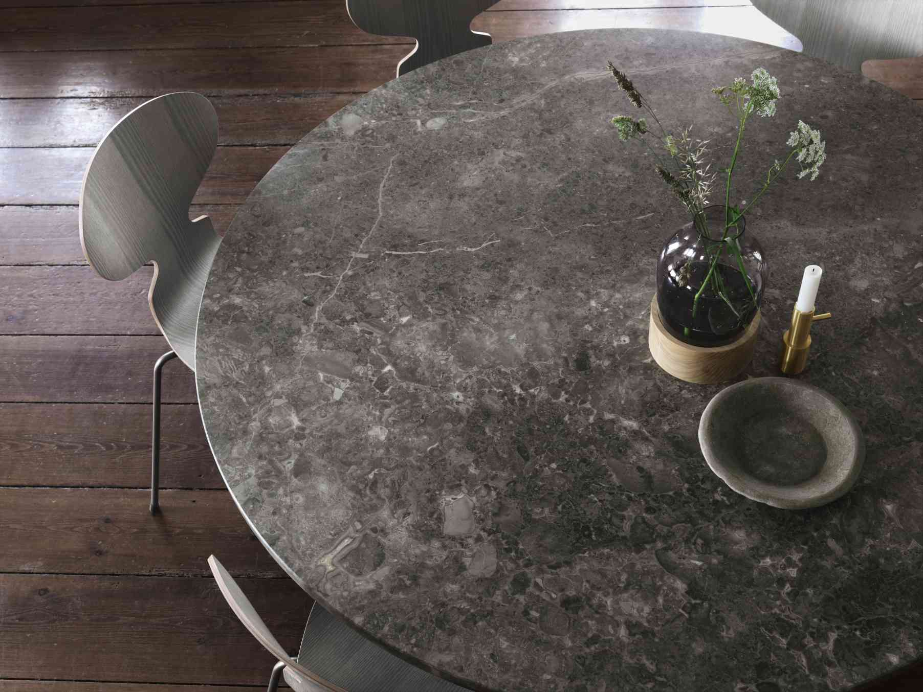 PK54 Esstisch von Fritz Hansen, runde Tischplatte aus Marmor mit Dekoration, Stühle im Hintergrund.