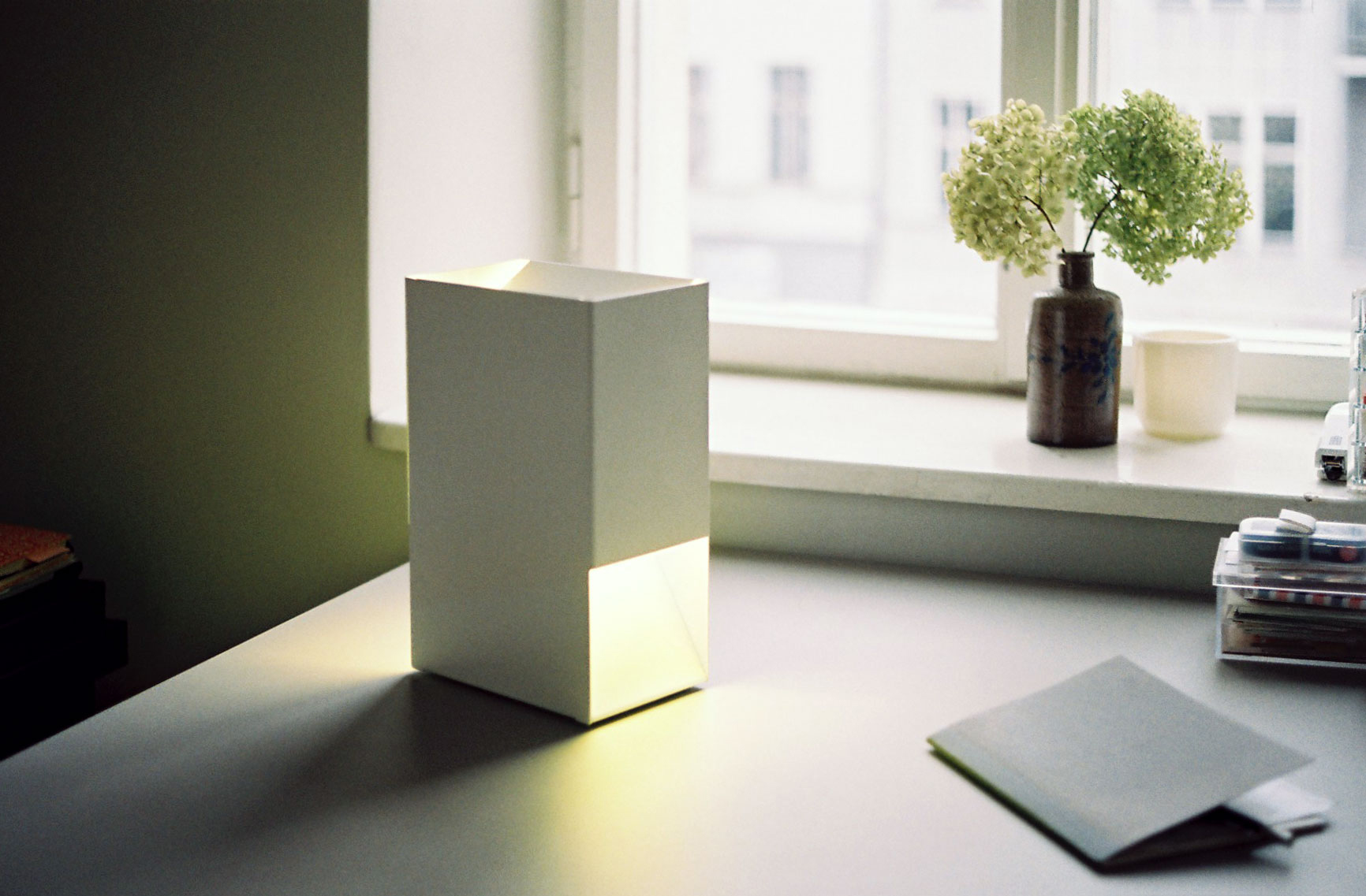 Weiße Linea1 Tischleuchte von Müller Möbelwerkstätten auf einem Schreibtisch, minimalistisches Design, stimmungsvolle Beleuchtung.