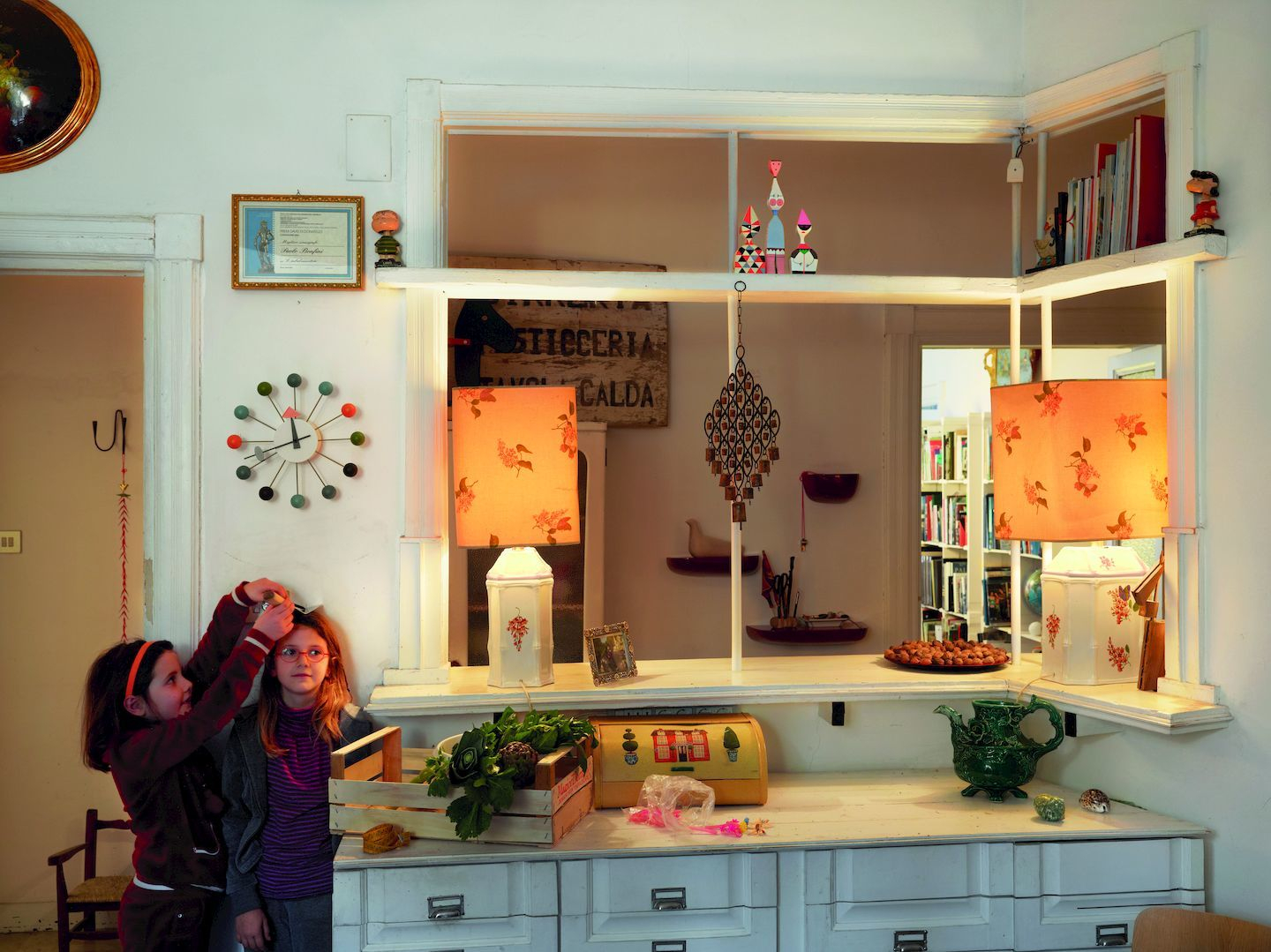 Zwei Mädchen vor einer Vitrine mit Holzfiguren, darunter eine Wooden Doll, und anderen Dekorationselementen.