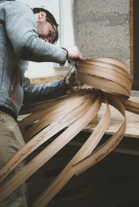 Mann fertigt handgefertigte Holzlampe aus gebogenen Holzstreifen in Werkstatt. Nachhaltige Holzleuchte.