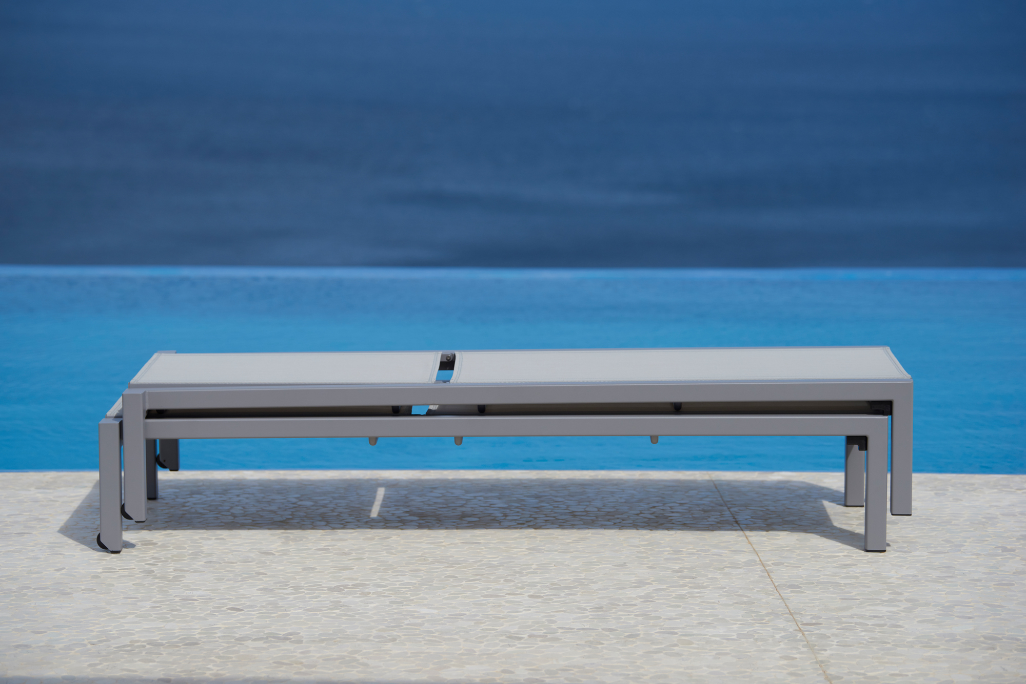 Stapelbare Cane-Line Sonnenliege "Relax Outdoor" in Grau vor blauem Pool und Meer.