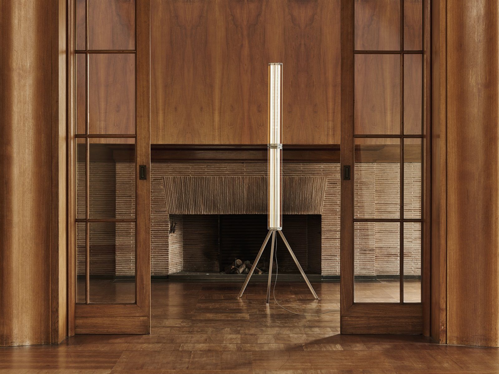 Superwire F Stehleuchte von Flos, moderne Innenbeleuchtung mit Tripod-Design vor Holzwand und Kamin.