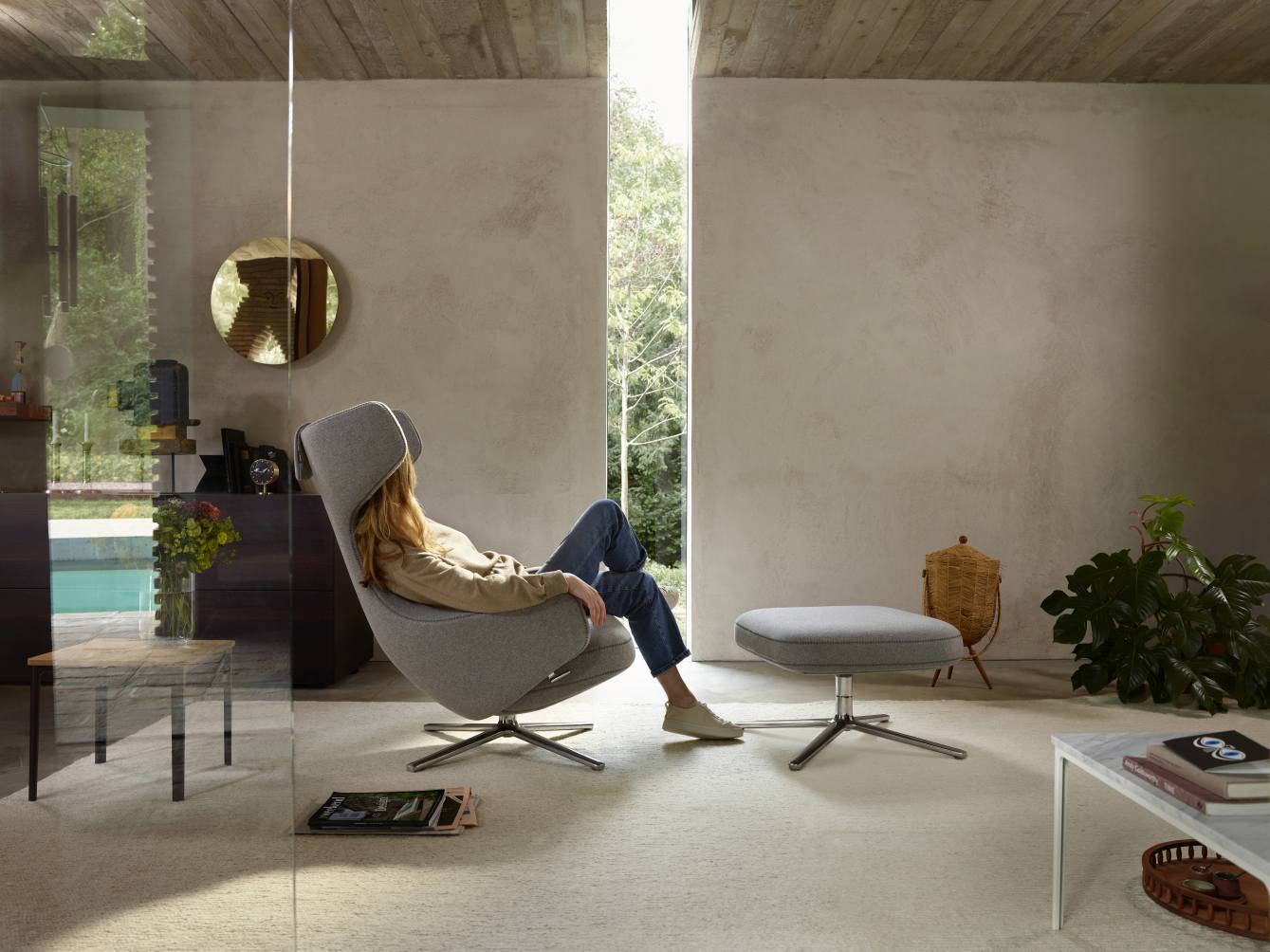 Frau entspannt im grauen Grand Repos Sessel mit Ottoman von Vitra, modernes Wohnzimmer Interieur.