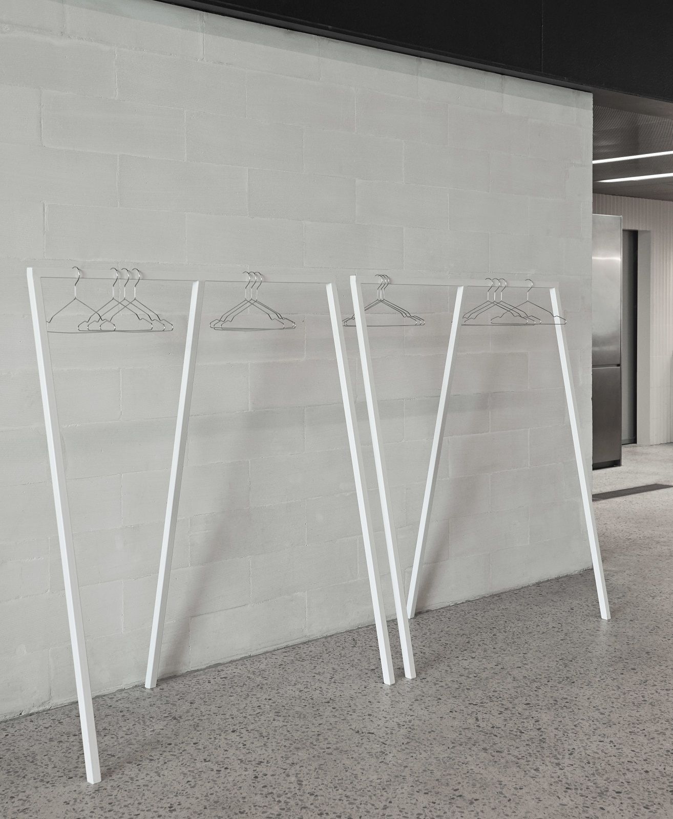 Weiße Loop Stand Garderobe von Hay mit minimalistischem Design und Kleiderbügeln vor einer hellen Wand.