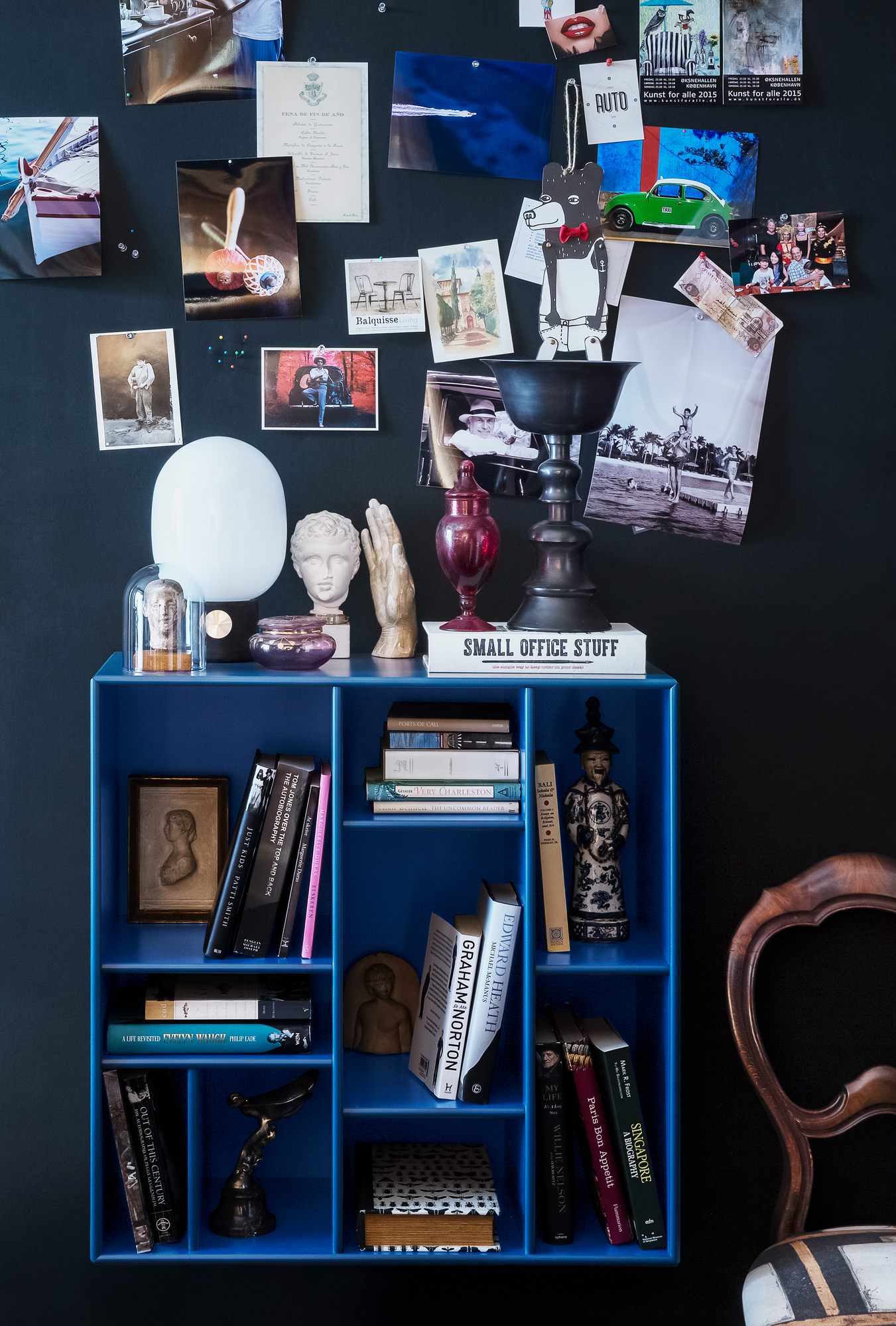 Blaues Compile Wandregal von Montana, gefüllt mit Büchern und Deko-Objekten vor schwarzer Wand.