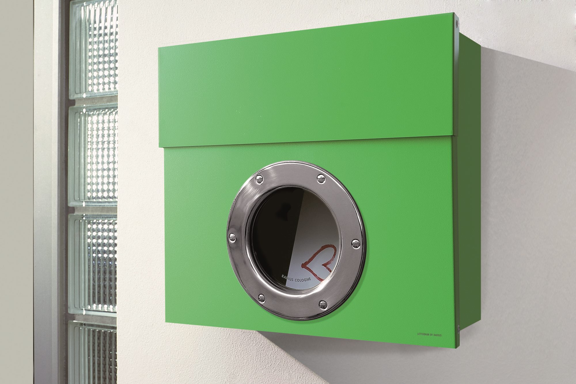 Grüner Letterman Briefkasten mit Bullauge und Edelstahlring an einer weißen Wand. Moderner Design-Briefkasten.