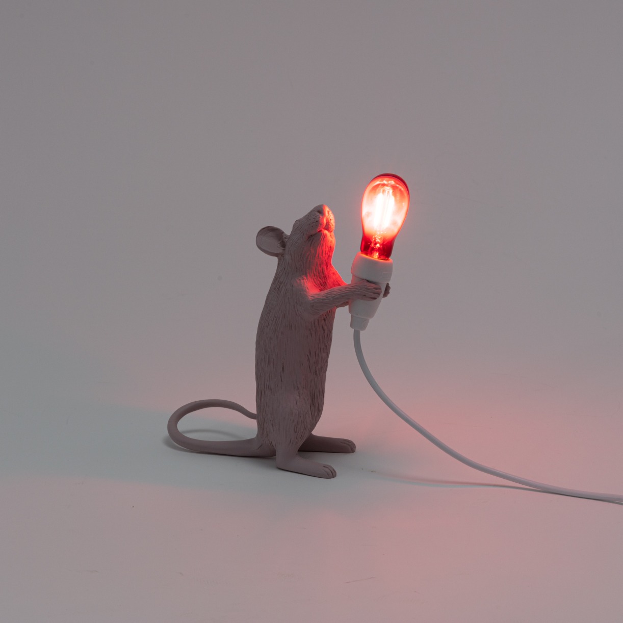 Seletti Mouse Lamp: Graue Maus hält eine leuchtende, rote Glühbirne als Tischleuchte.
