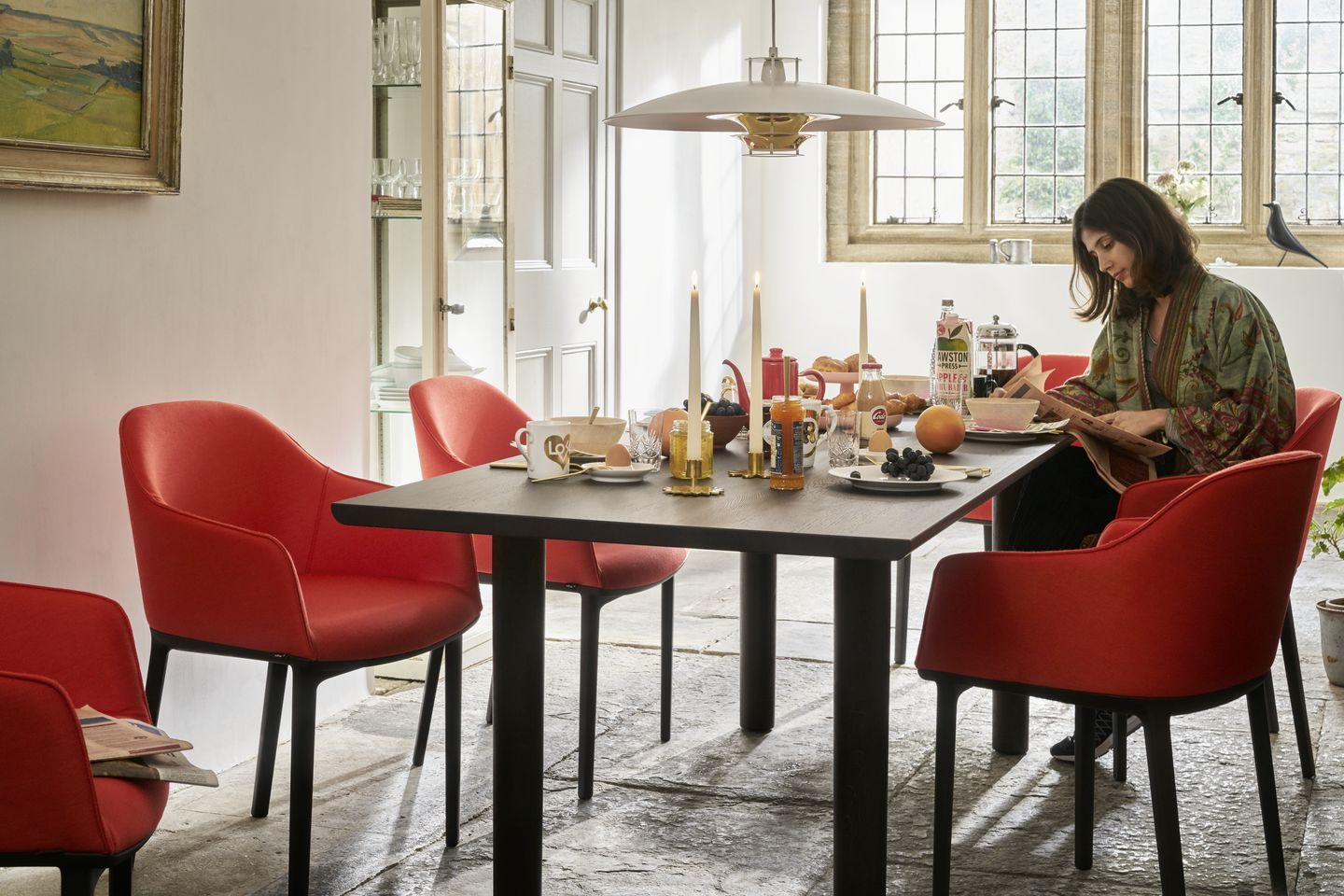 Esszimmer mit Vitra Softshell Chairs in Rot und einer Person beim Frühstück am Tisch.