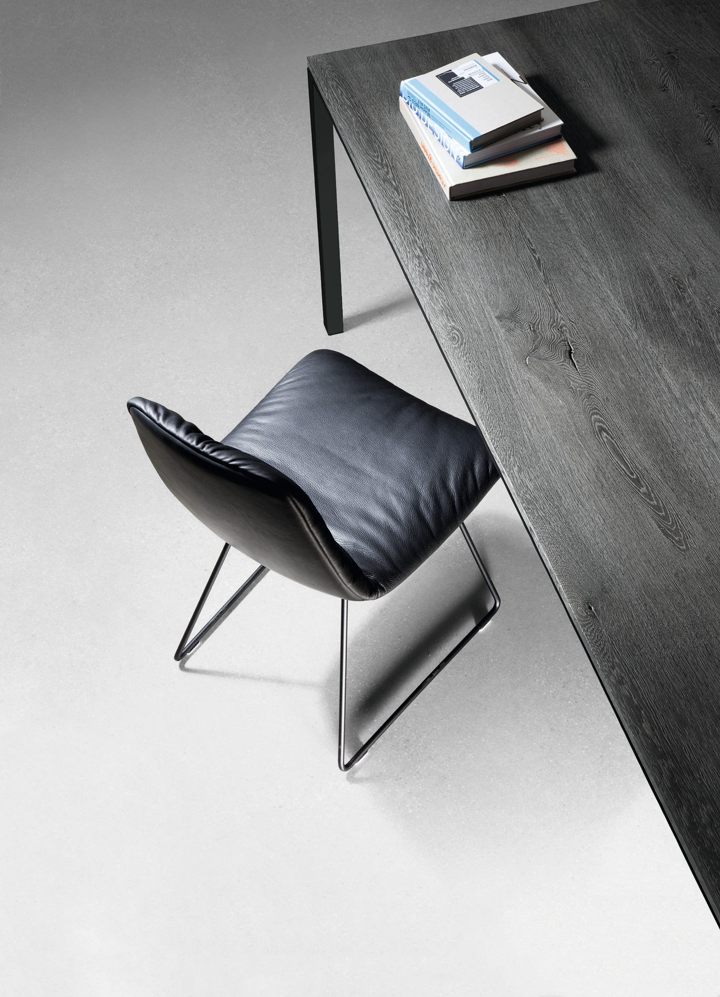 Detailaufnahme vom Janua S 600 Tisch Eiche geköhlt mit schwarzem Lederstuhl und Büchern.