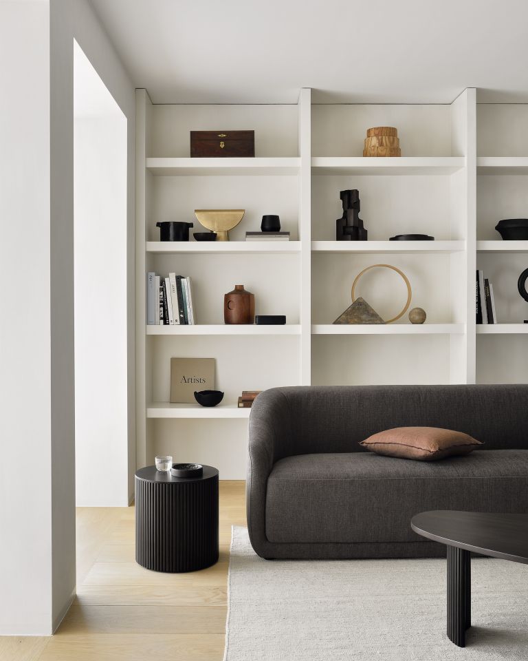 Dunkelbrauner Ethnicraft Roller Max Beistelltisch rund im modernen Wohnzimmer mit Sofa und Bücherregal.
