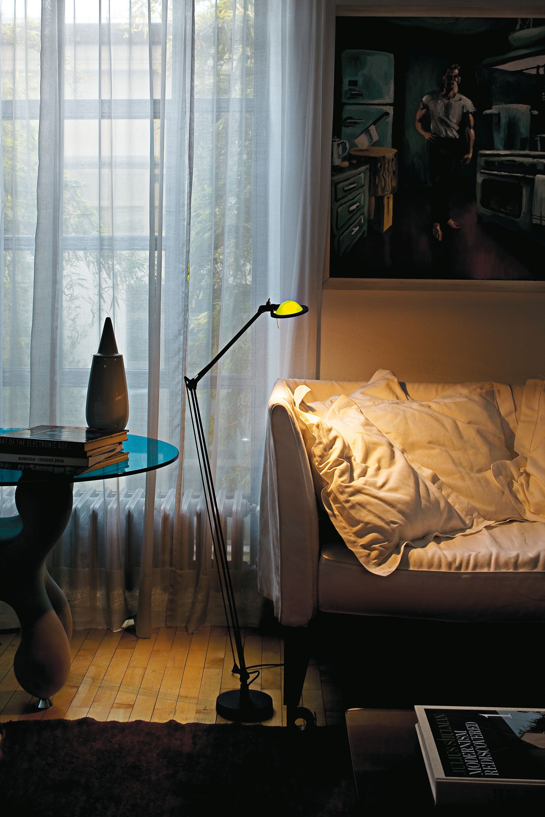 Schwarze D12 Berenice Stehleuchte von Luceplan im Wohnzimmer, mit gelbem Lichtschein auf dem Sofa.