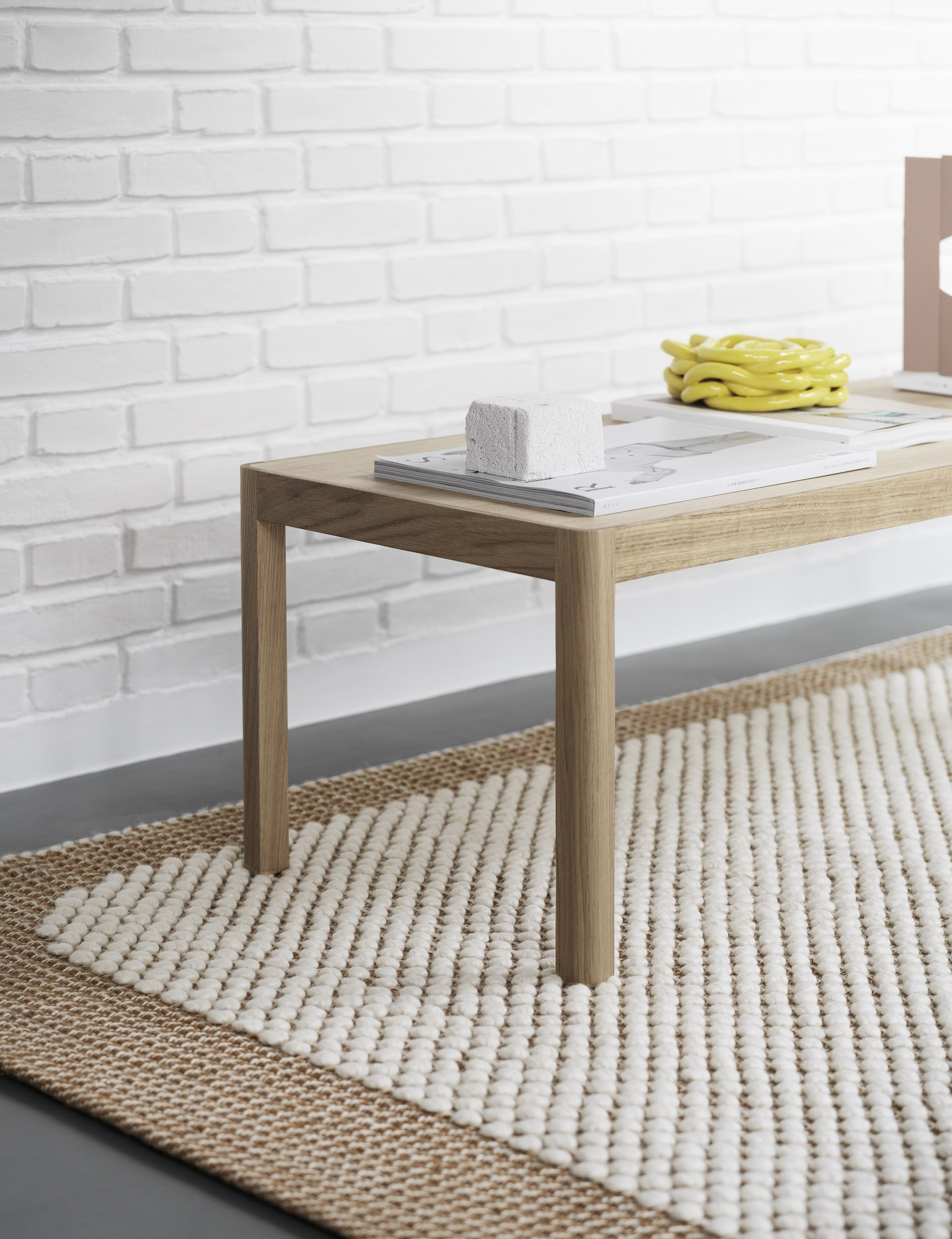 Detailaufnahme des Muuto Pebble Rug Teppichs in Beige und Weiß unter einem Holztisch.