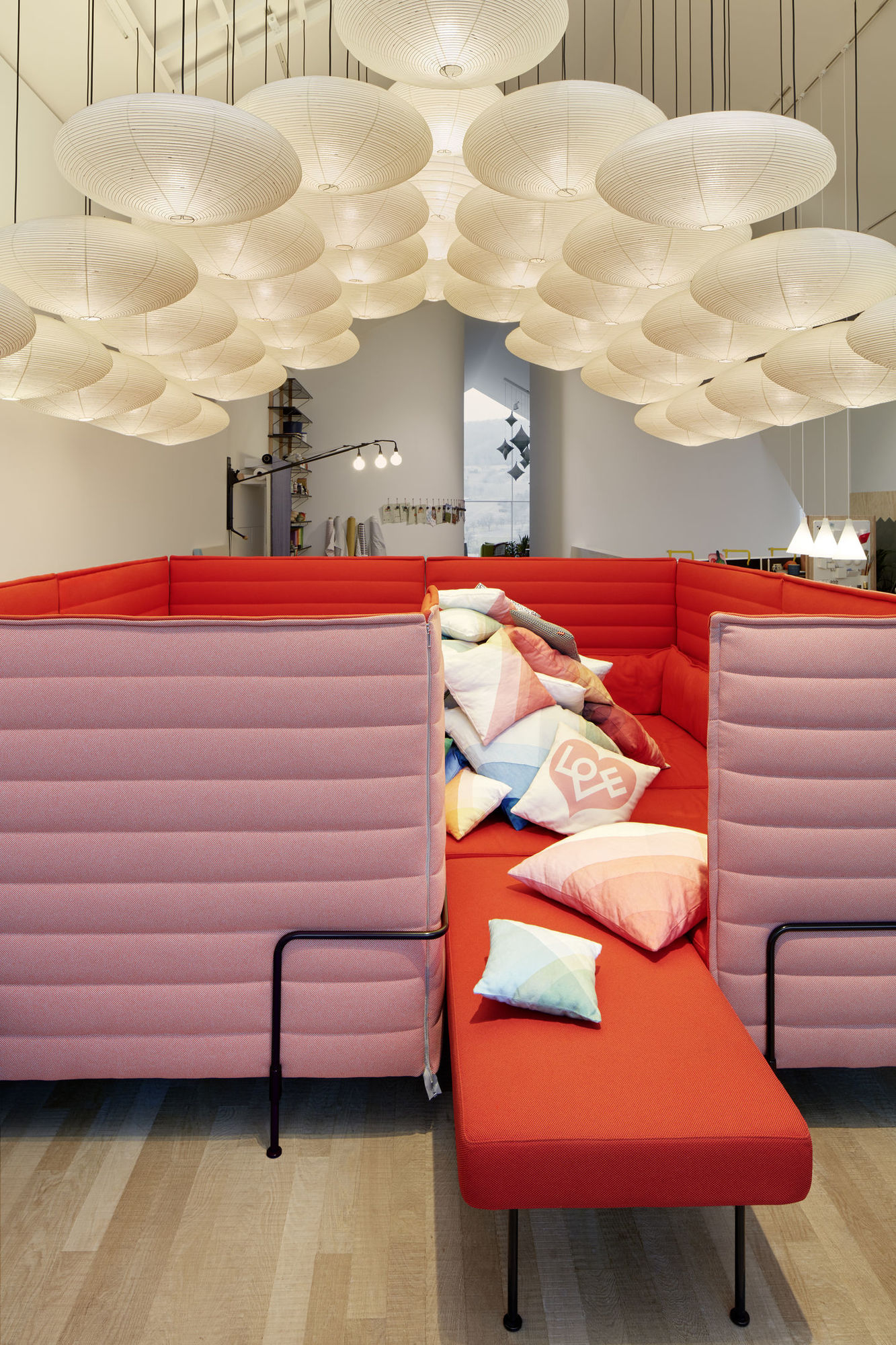 Raum mit roter Sitzecke und vielen Akari Leuchten von Vitra, die von der Decke hängen.
