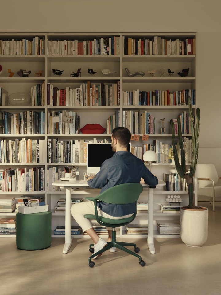 Mann sitzt auf einem grünen Vitra Bürodrehstuhl mit Mynt Polsterung vor einem Schreibtisch in einem Büro.