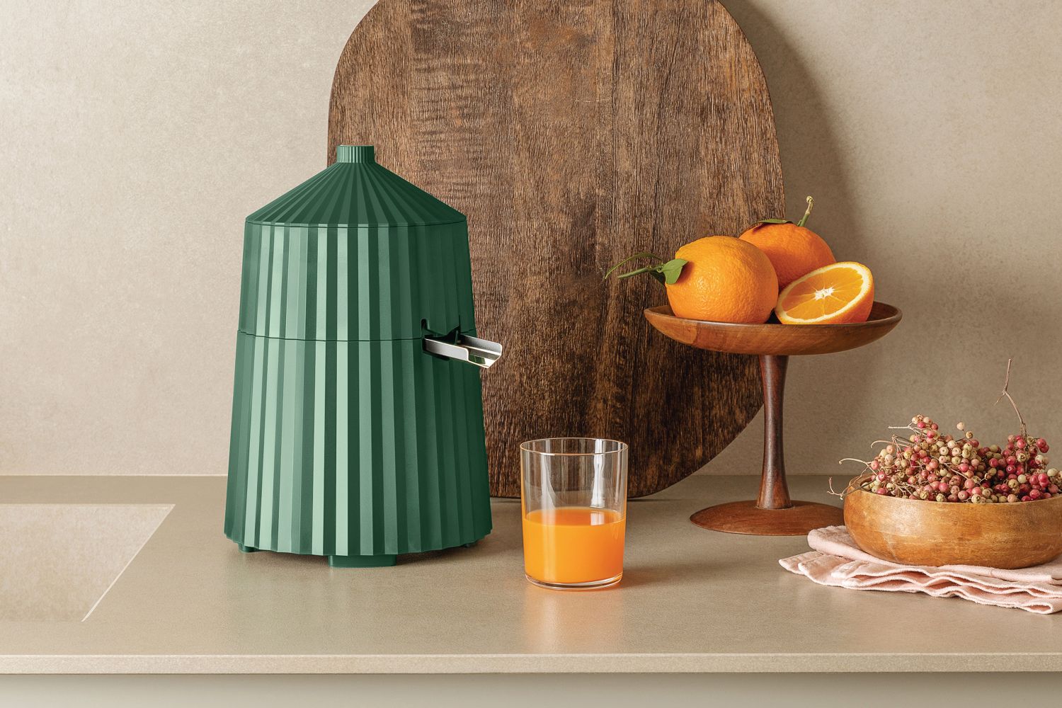 Grüne Alessi Zitronenpresse mit Plissee-Design, frischem Orangensaft und Orangen auf einem Holztisch.