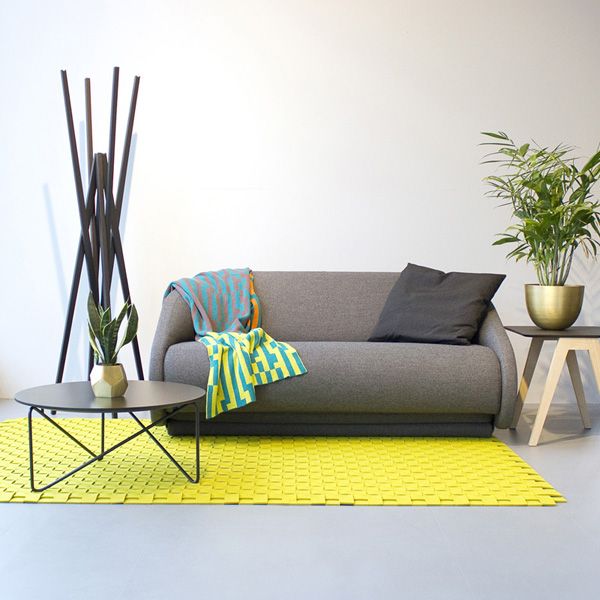 Graues Up-lift Schlafsofa von Prostoria mit Kissen und Decken auf gelbem Teppich im modernen Wohnzimmer.