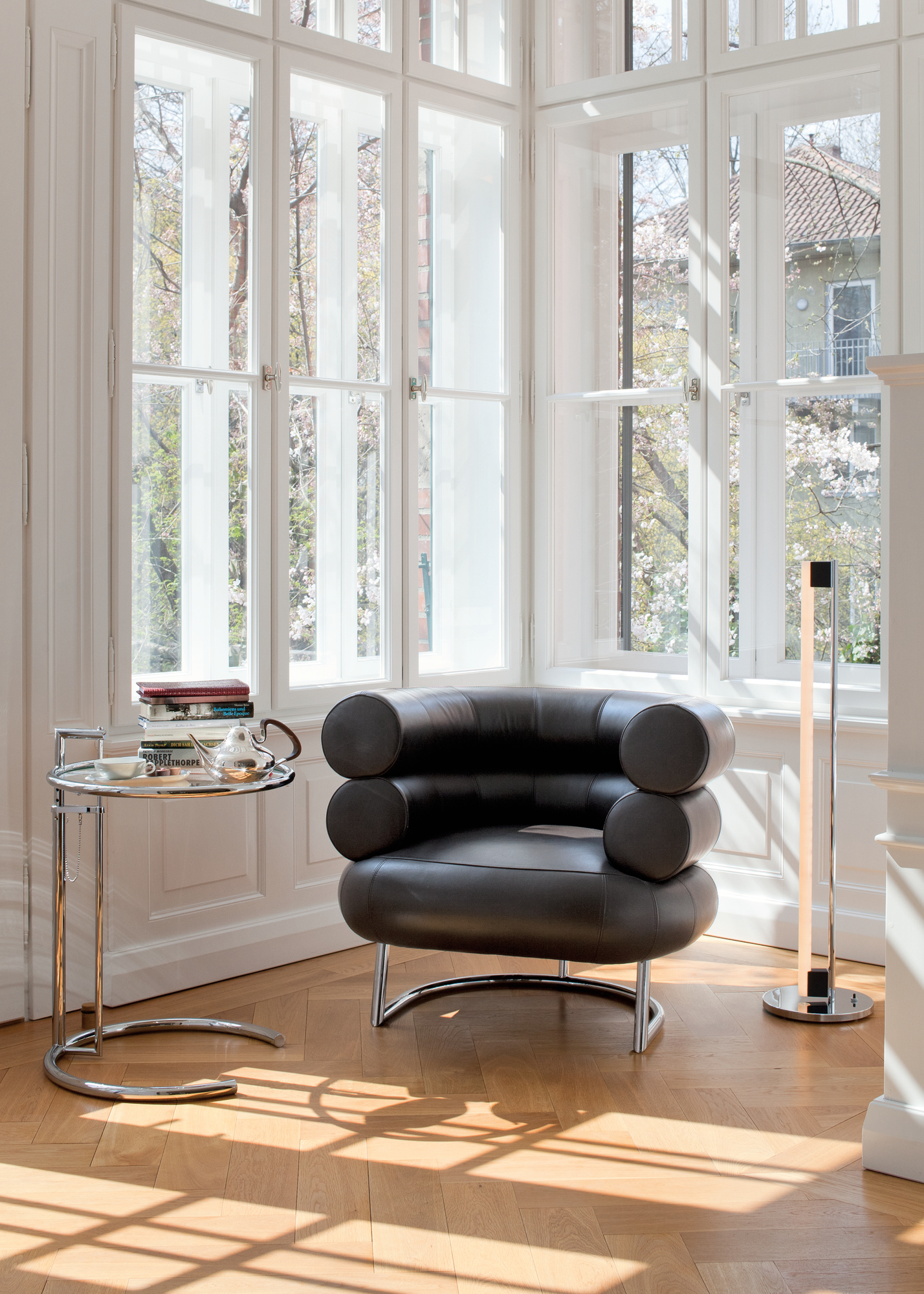 Nahaufnahme des ClassiCon Adjustable Table E1027 Beistelltischs neben einem Sessel und einer Stehlampe in einem hellen Raum.