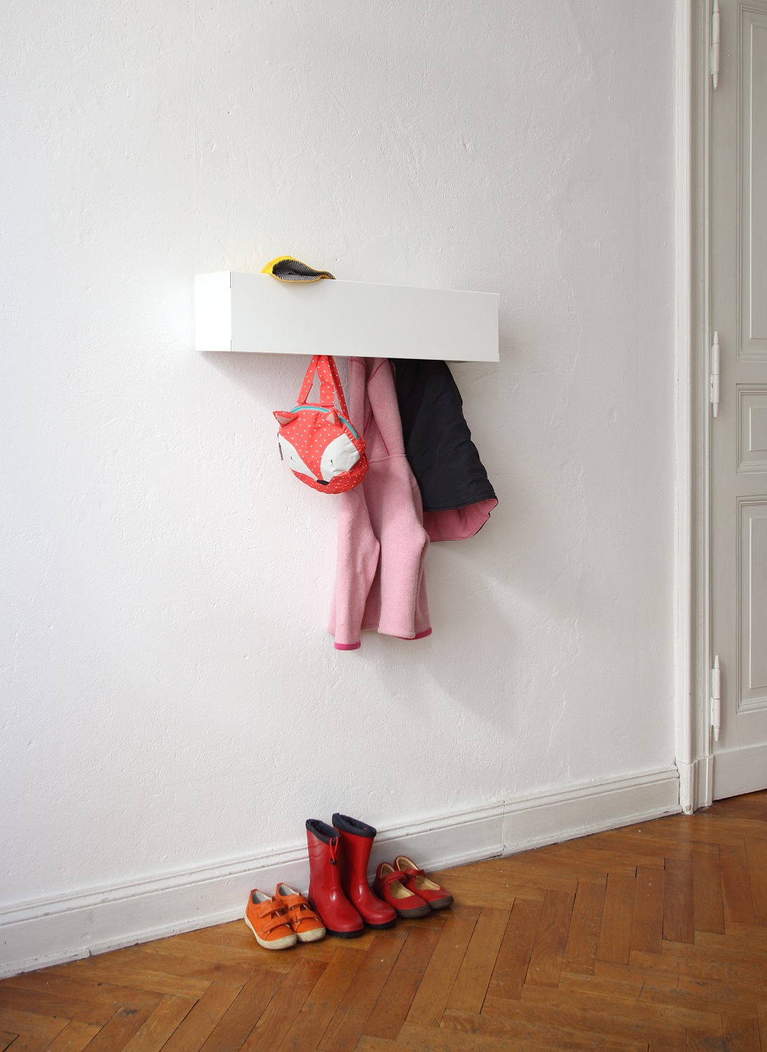 Weiße Wandgarderobe CR Linea1 von Müller Möbelwerkstätten mit Kinderkleidung und Schuhen an einer weißen Wand.