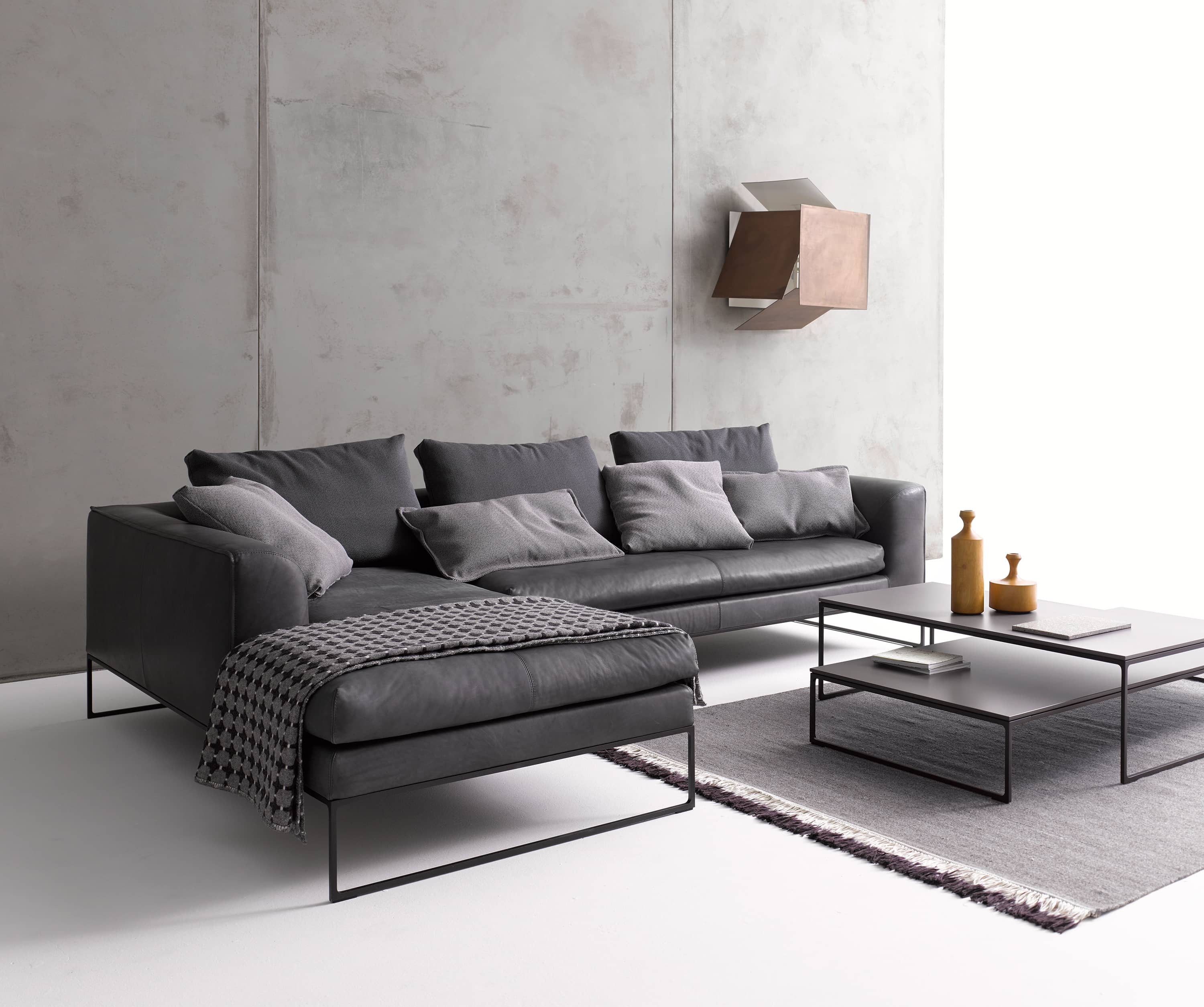 Graue Ledercouch mit Ottomane und Kissen, minimalistischer Couchtisch und Teppich im modernen Wohnzimmer.
