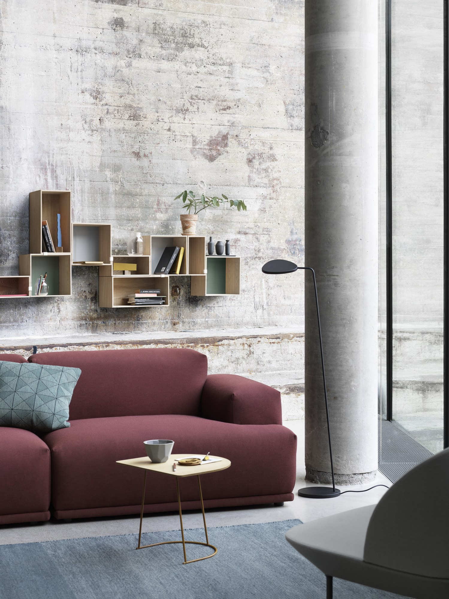 Moderne Muuto Leaf Floor Lamp Stehleuchte im Wohnzimmer mit Sofa, Tisch und Regalen vor Betonwand.