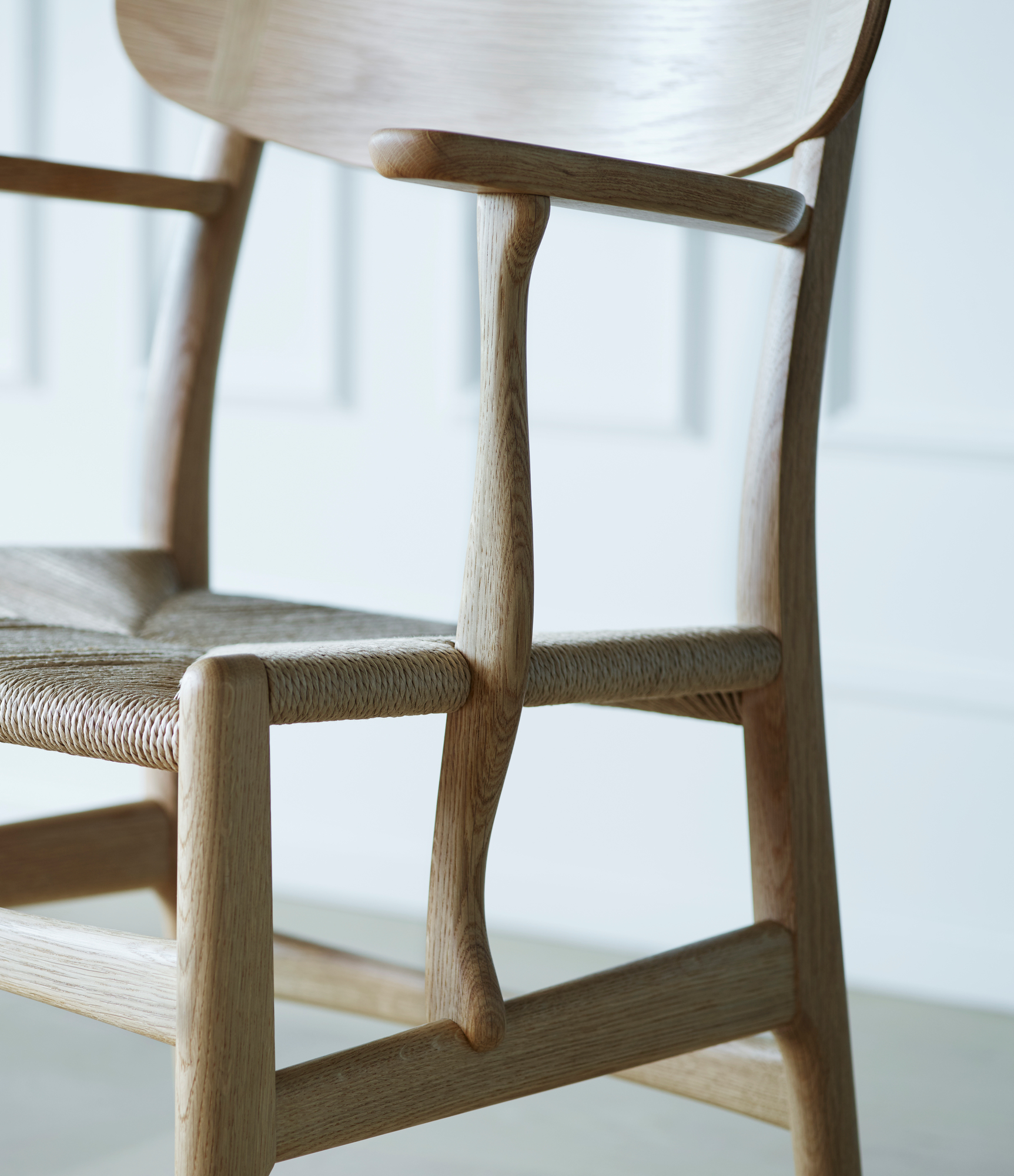 Detailaufnahme des CH26 Holzstuhls von Carl Hansen & Søn mit geflochtener Sitzfläche und Armlehnen.