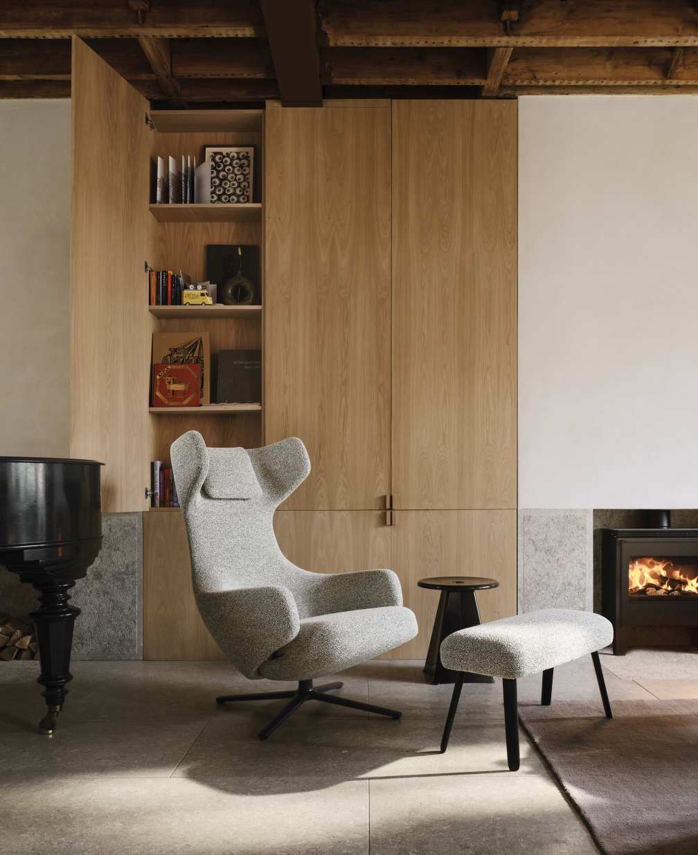 Vitra Grand Repos Sessel mit Ottoman in Kiesel Melange vor modernem Kamin und Holzschrank.
