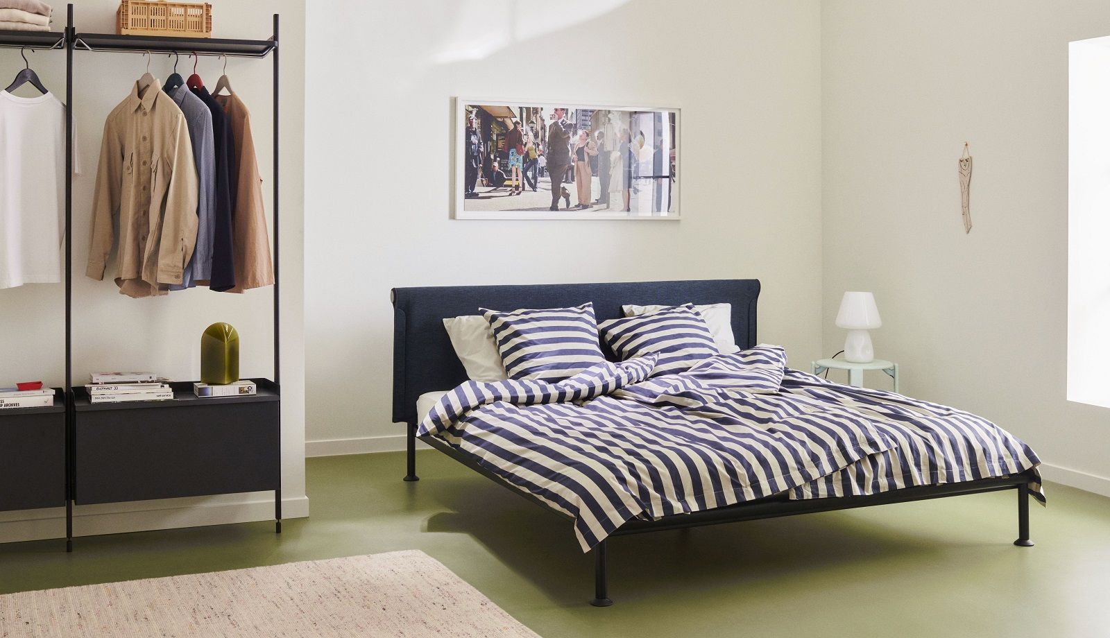 Helles Schlafzimmer mit Hay Pier System Regal, Kleidung und Bett mit blau-weiß gestreifter Bettwäsche.
