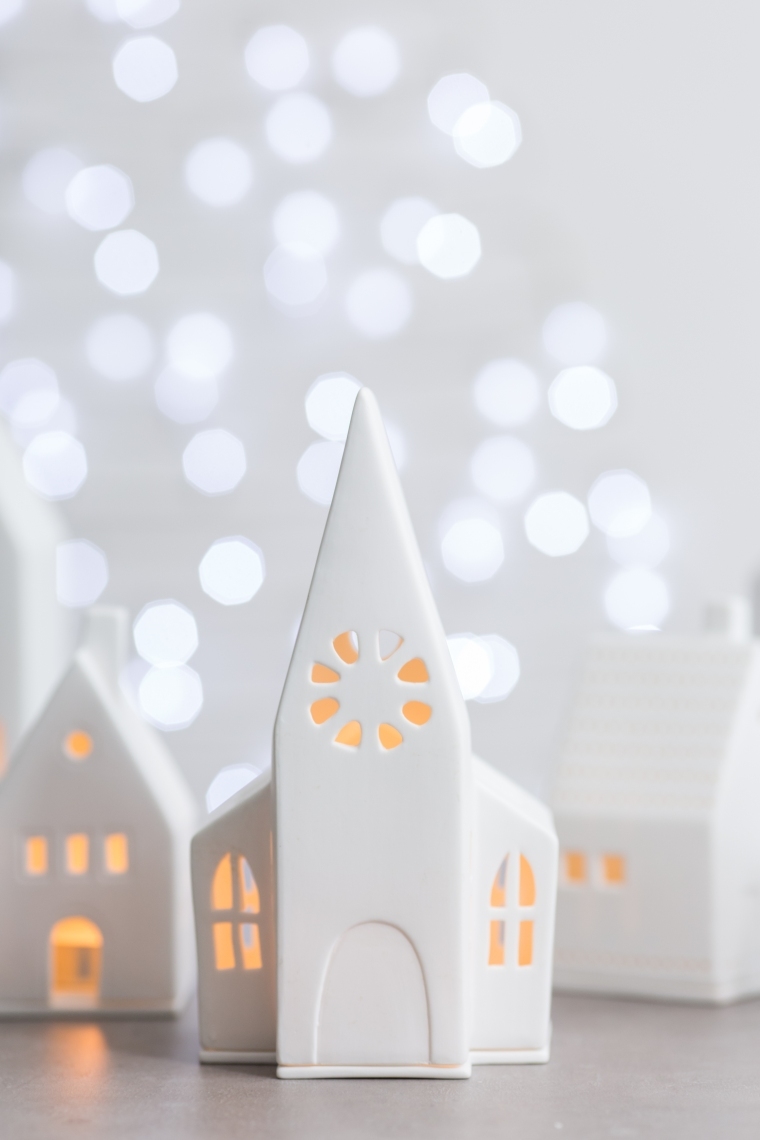 Weißes Lichthaus in Kirchenform mit warmem Licht und Bokeh im Hintergrund. Dekorative Häuser für Weihnachten.