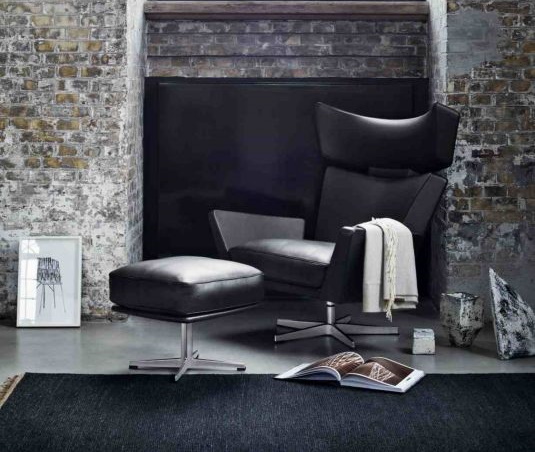 Schwarzer Ledersessel mit Hocker und silbernem Fußkreuz, modernes Design für Wohnzimmer und Büro.