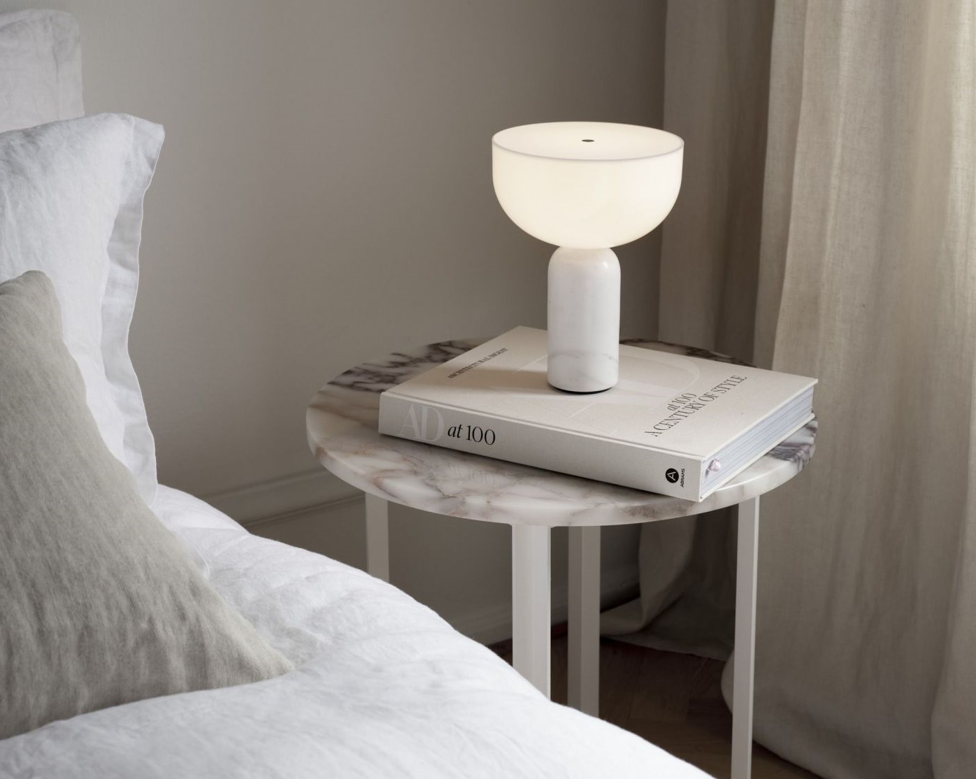 Weiße Tischleuchte mit Marmorfuß auf Nachttisch mit Buch im Schlafzimmer. Moderne Nachttischlampe für stimmungsvolle Beleuchtung.