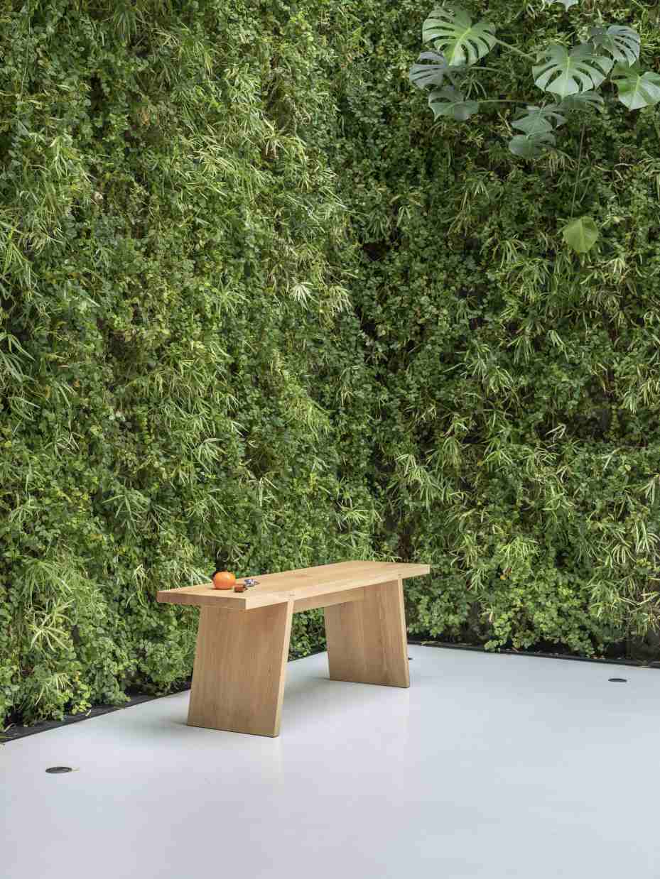 Hölzerne Dovetail Bank vor grüner Wand. Moderne Gartenbank für den Außenbereich.