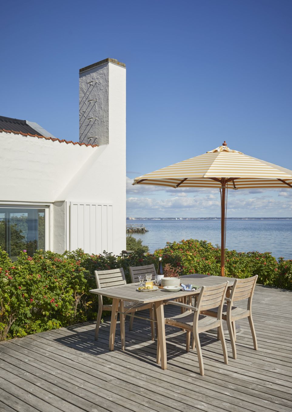 Outdoor-Szene mit Ballare Chair Stühlen von Skagerak by Fritz Hansen auf einer Holzterrasse am Meer.