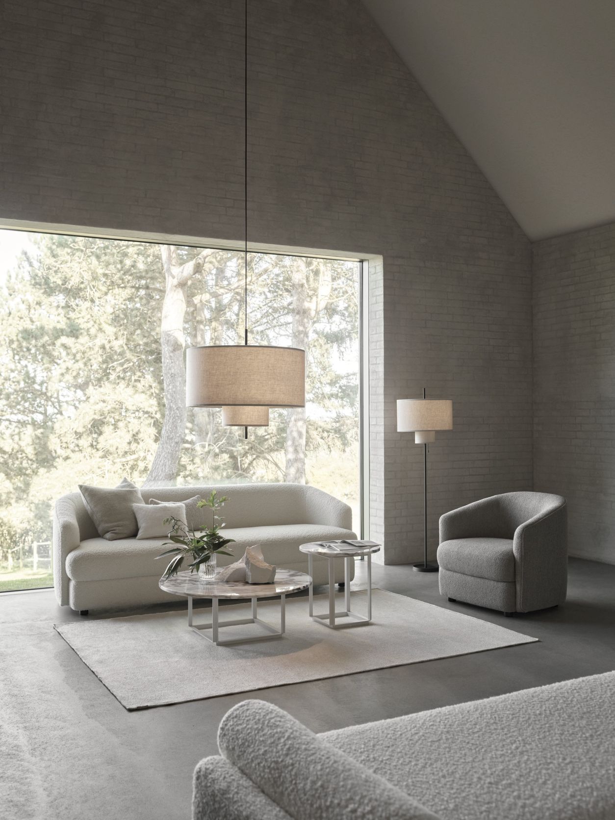 Helle Wohnzimmer-Szene mit New Works Margin Pendelleuchte, Sofa, Sessel und Beistelltischen vor großem Fenster.