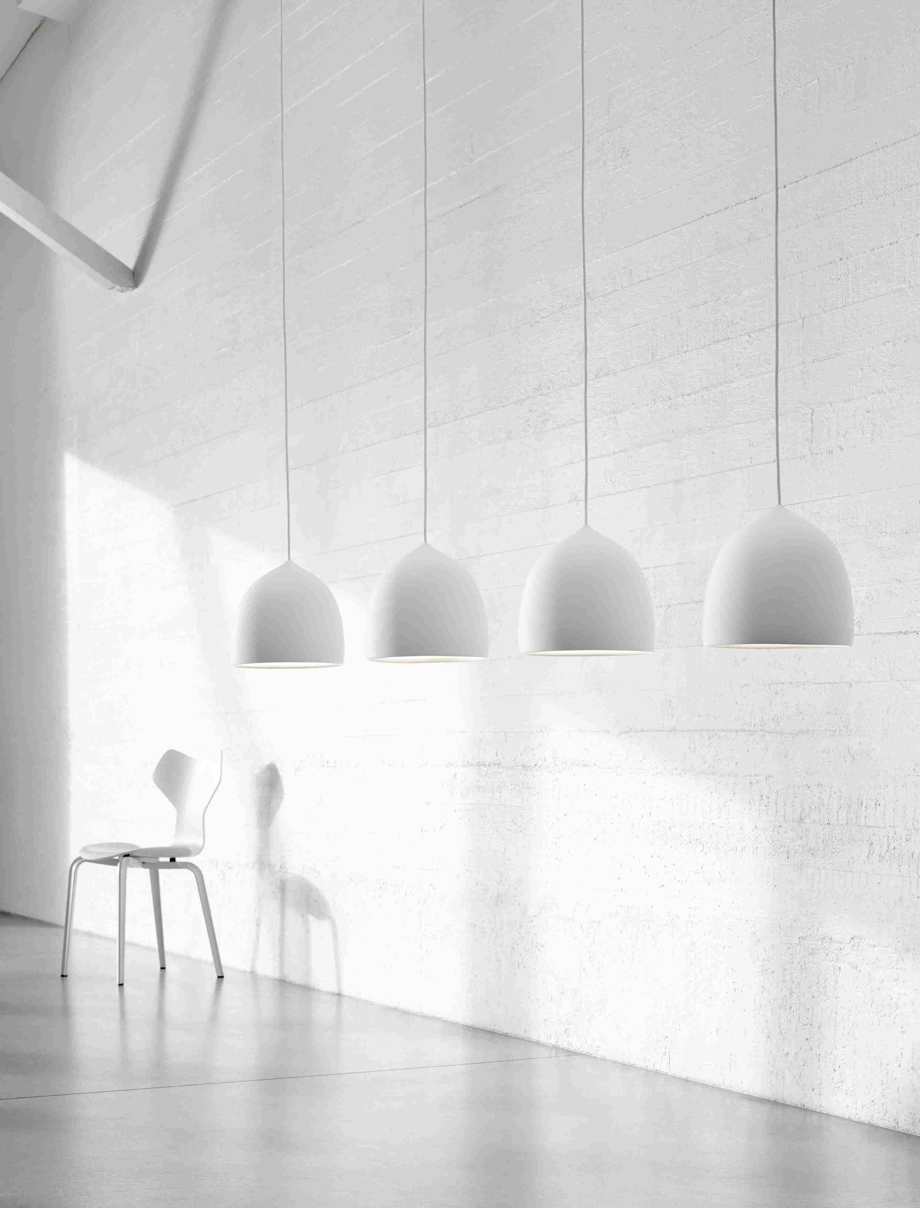 Weißer Grand Prix Stuhl von Fritz Hansen vor weißer Wand und vier Hängelampen.