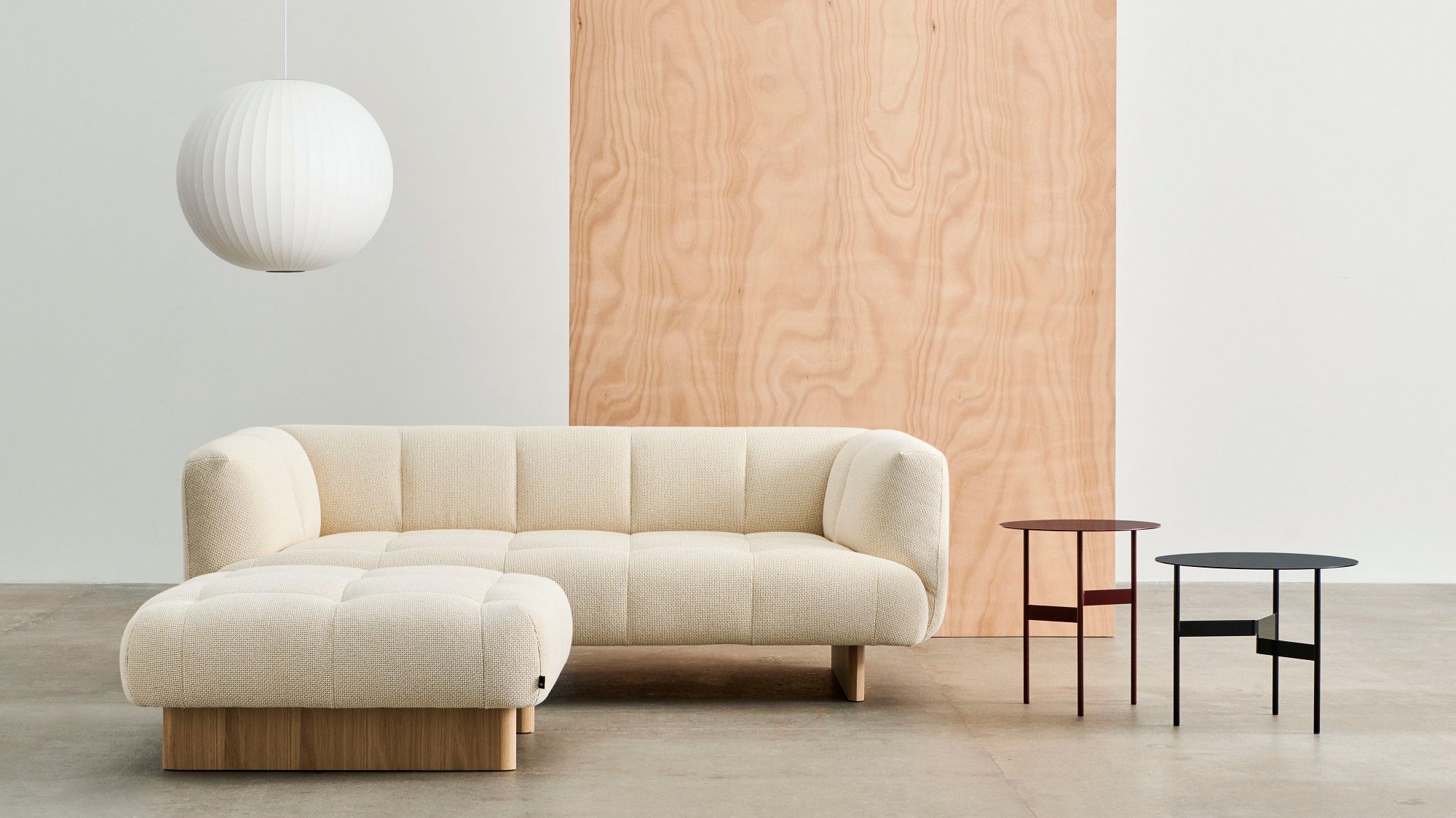 Beiger Quilton Ottoman Hocker von Hay mit Stoffbezug und Holzsockel im modernen Wohnzimmer.