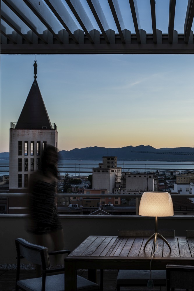 Lumiere Tischleuchte von Foscarini auf einem Holztisch mit Stadtblick im Hintergrund, stimmungsvolle Beleuchtung.