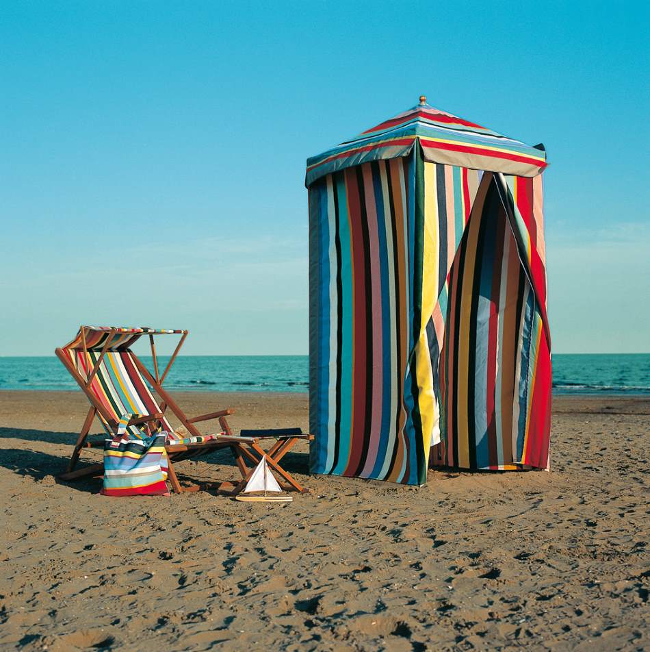 Weishäupl Cabin Outdoor Liegestuhl Deluxe mit farbenfrohem Strandzelt und Dekoration am Meer.