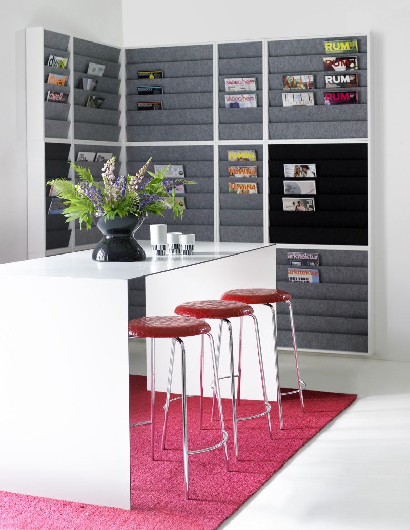 Heller Raum mit Karl Andersson & Soener Thinner Tisch, roten Barhockern und Zeitschriftenregal.