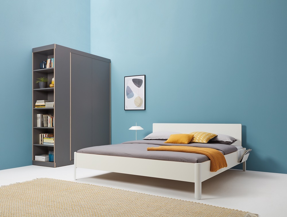 Nait Bett CPL Weiß von Müller Möbelwerkstätten mit grauem Schrank und Teppich auf blauem Hintergrund.
