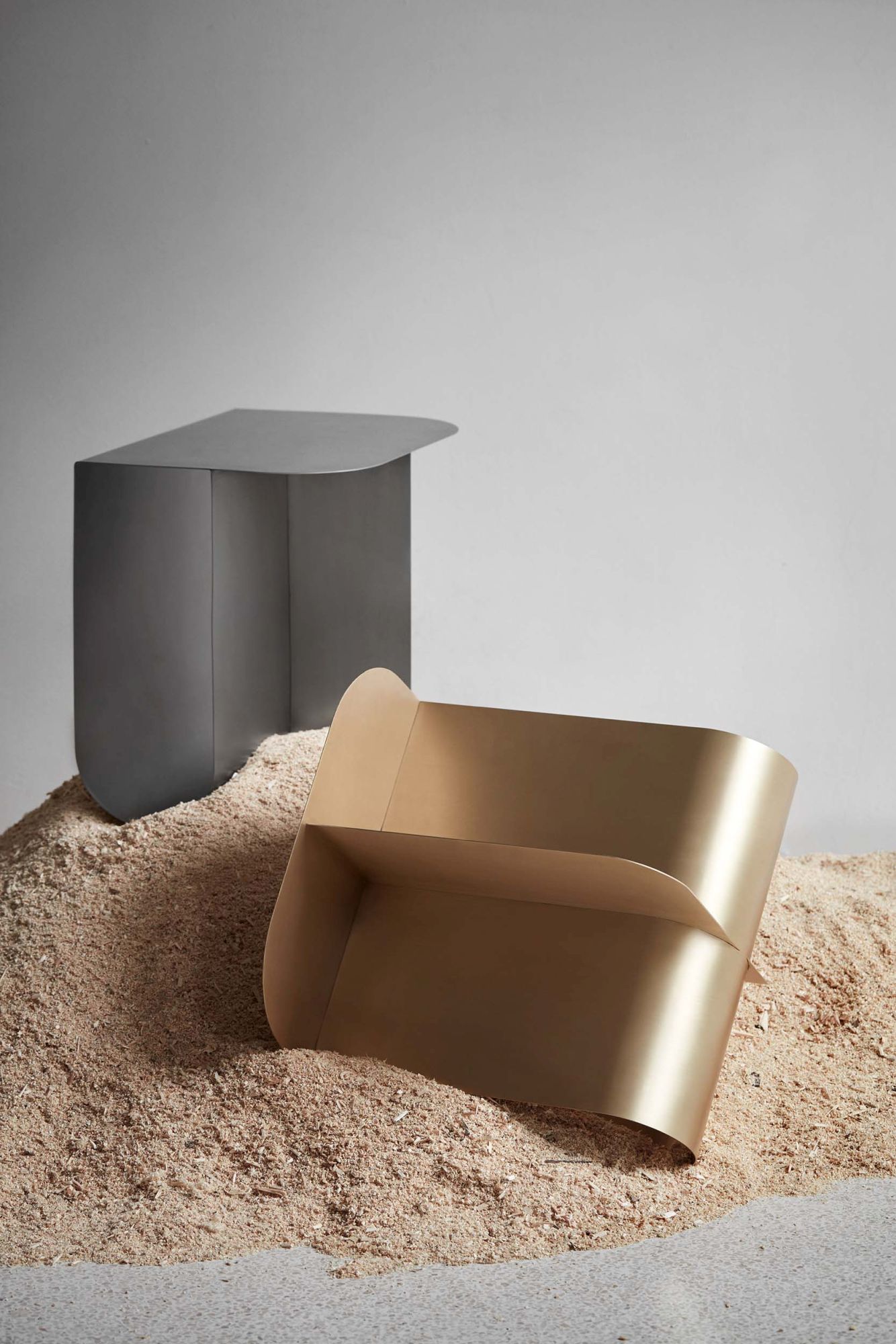 Zwei Mass Beistelltische aus Stahl in Grau und Gold auf Sandhaufen. Modernes Design.