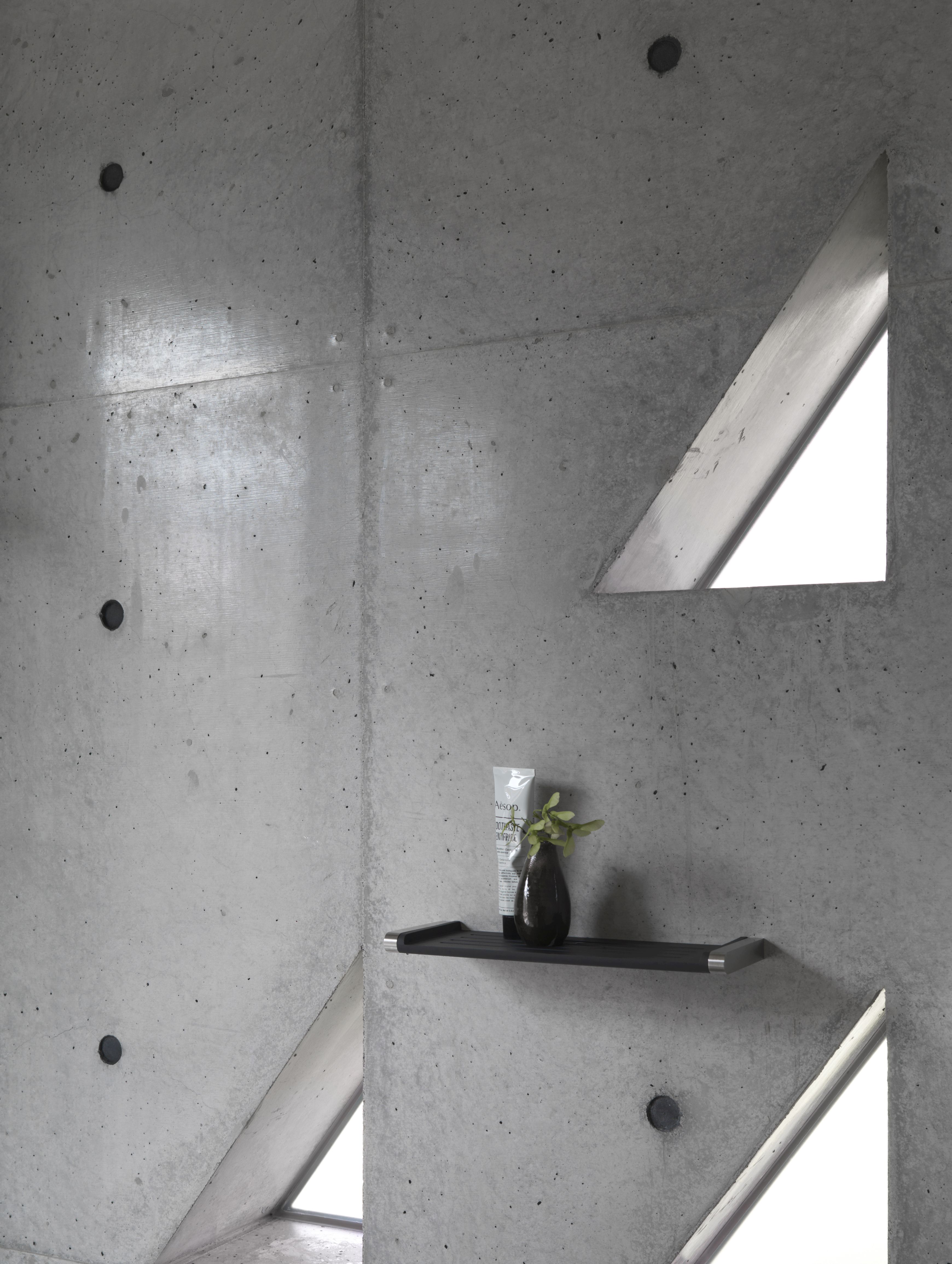 Schwarze Vipp Badablage an Betonwand mit Badutensilien und dreieckigem Fenster. Minimalistisches Badezimmer Design.