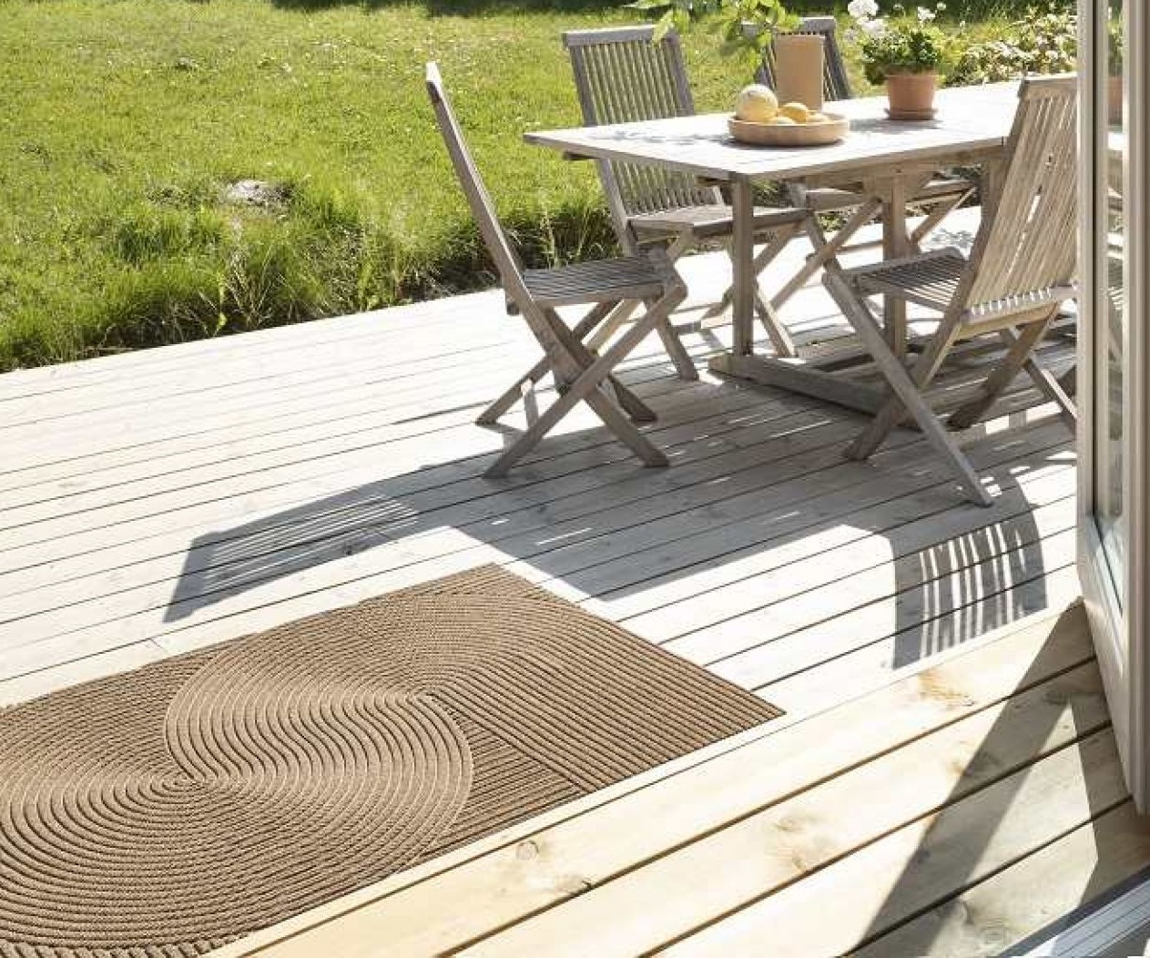Brauner Outdoor Teppich mit Spiralmuster auf einer Holzterrasse mit Gartenmöbeln im Hintergrund.