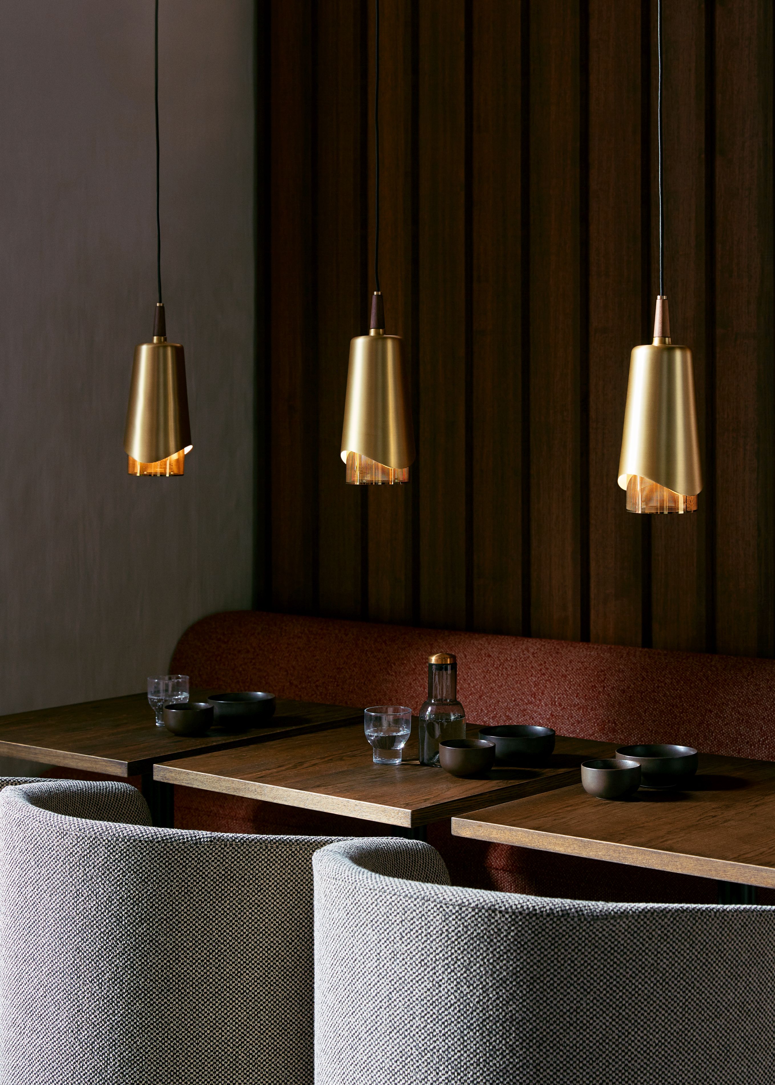 Drei goldene Umanoff Pendelleuchten von Audo über einem gedeckten Holztisch in einem Restaurant.