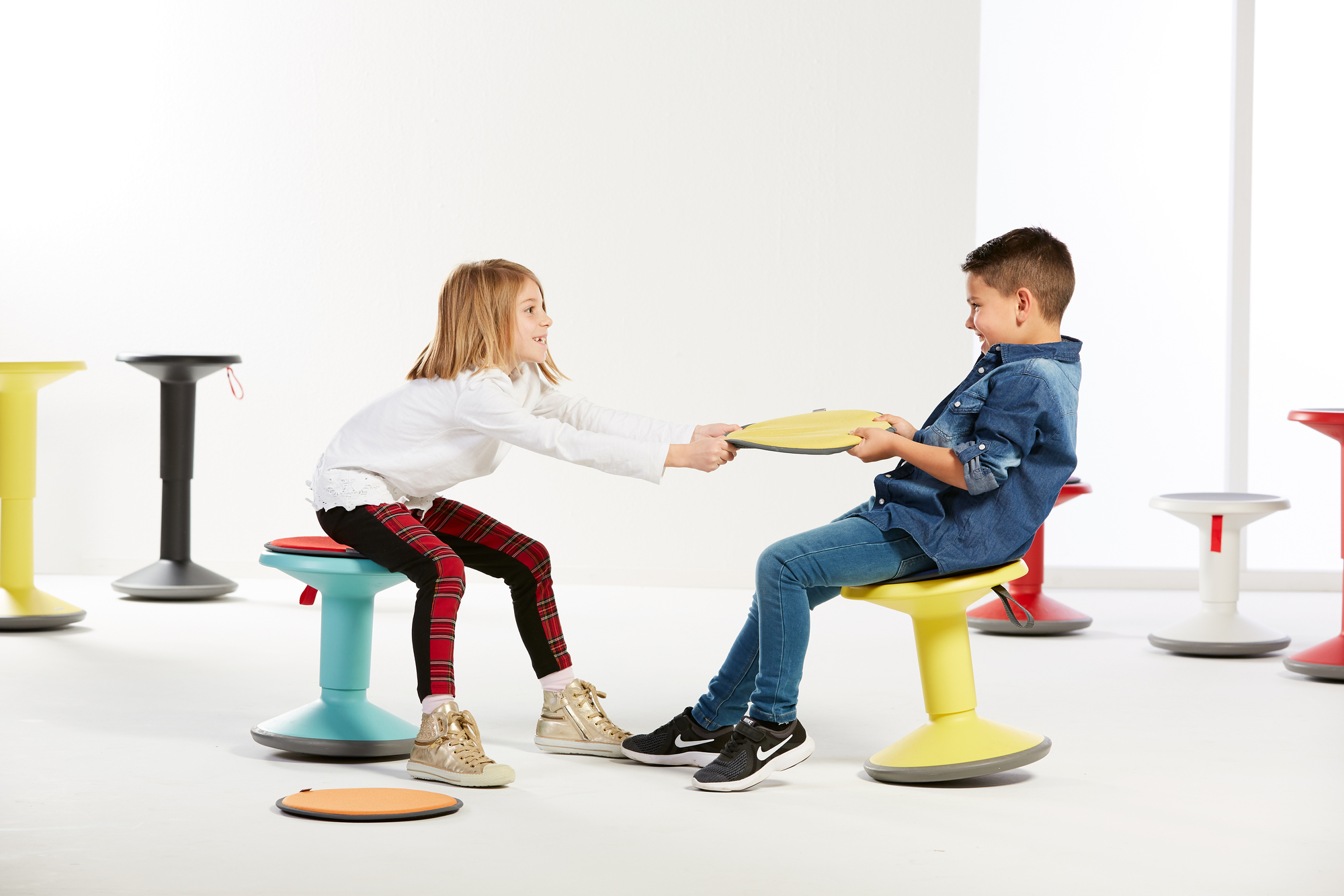 Zwei Kinder spielen auf bunten Interstuhl UP Junior Edition Kinderhockern, einer davon in Lachsorange.