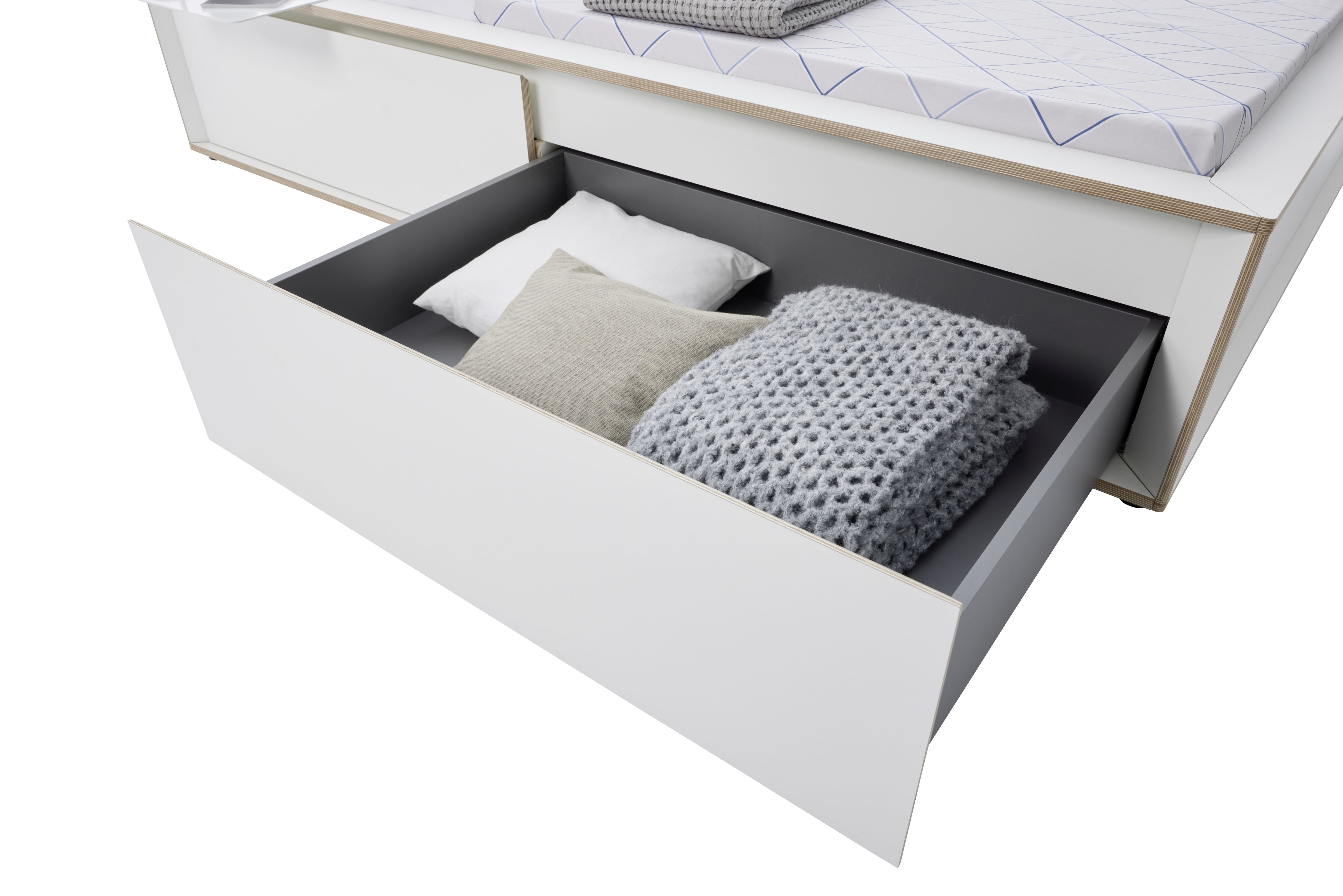 Spaze Bett von Müller Möbelwerkstätten mit offener Schublade, gefüllt mit Kissen und einer grauen Strickdecke.