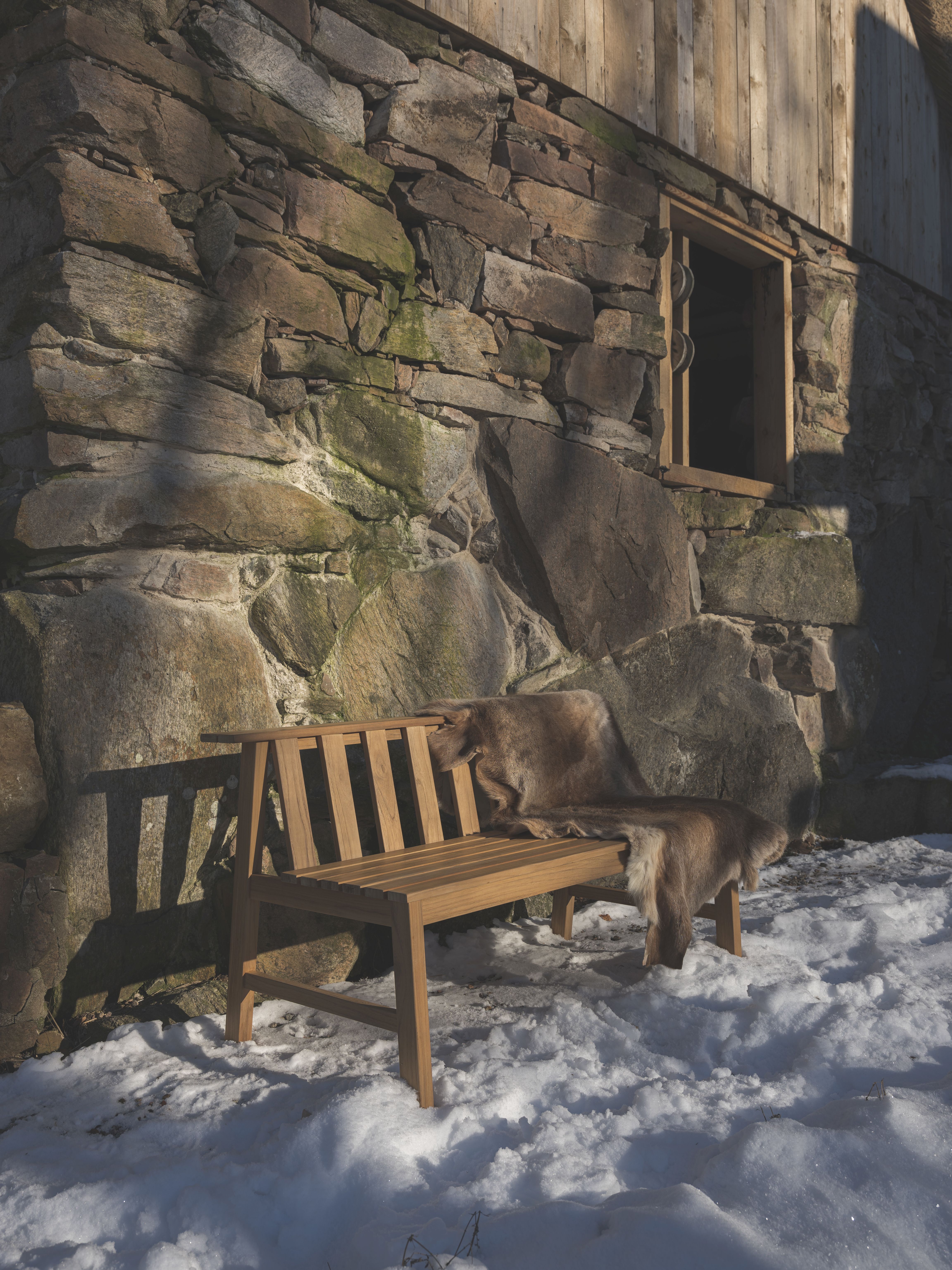Cadence Bank Teak Outdoor Bank von Fritz Hansen mit Fell auf Schnee vor Steinwand.